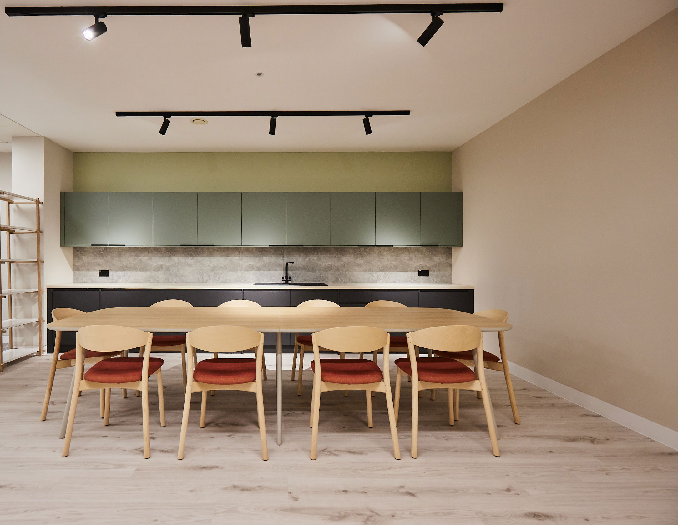 A large minimalistic wooden table and chairs fill a kitchen and office tea point area