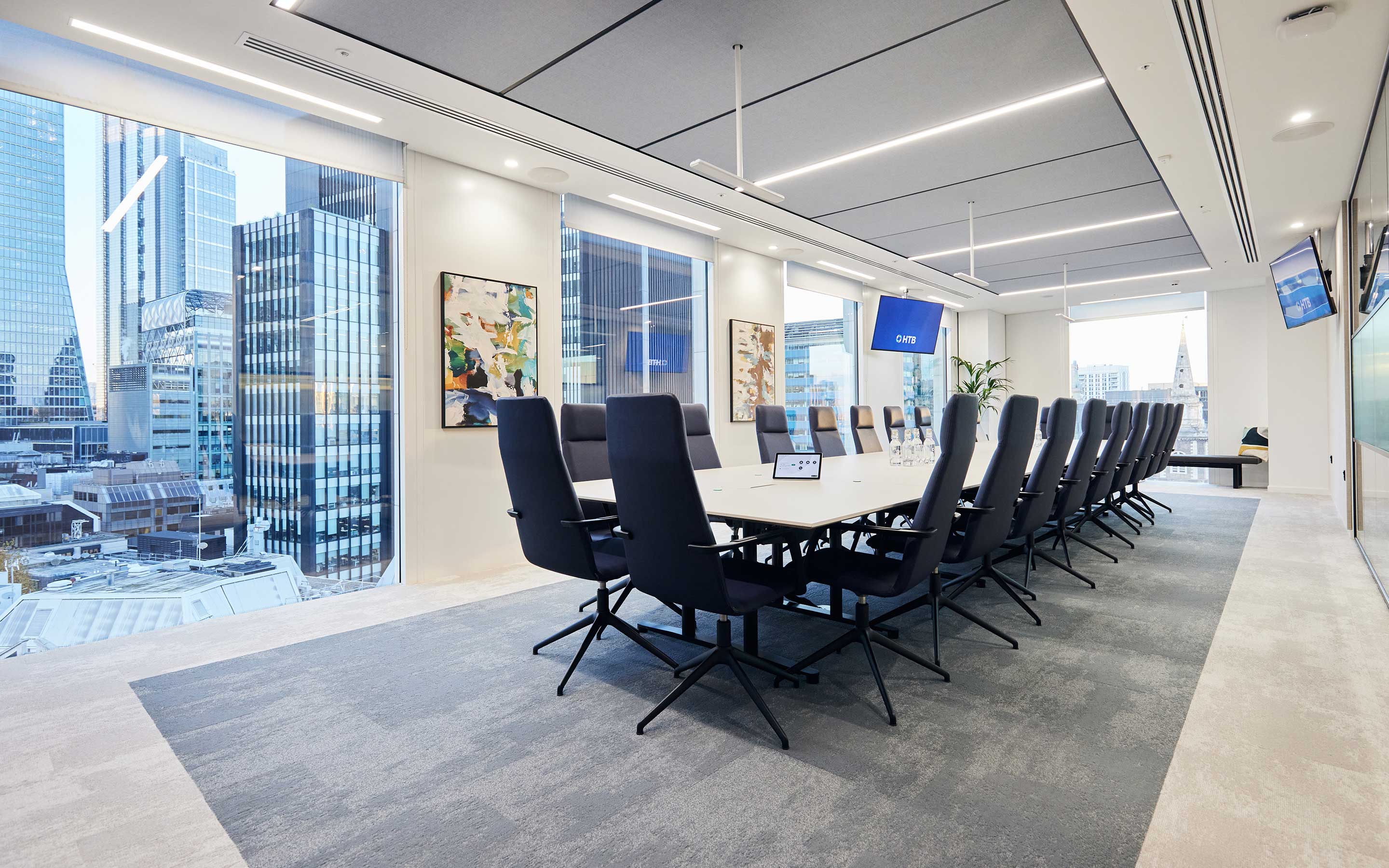A sleek conference room and boardroom table with acoustic panels, a plush carpet, and lovely city views
