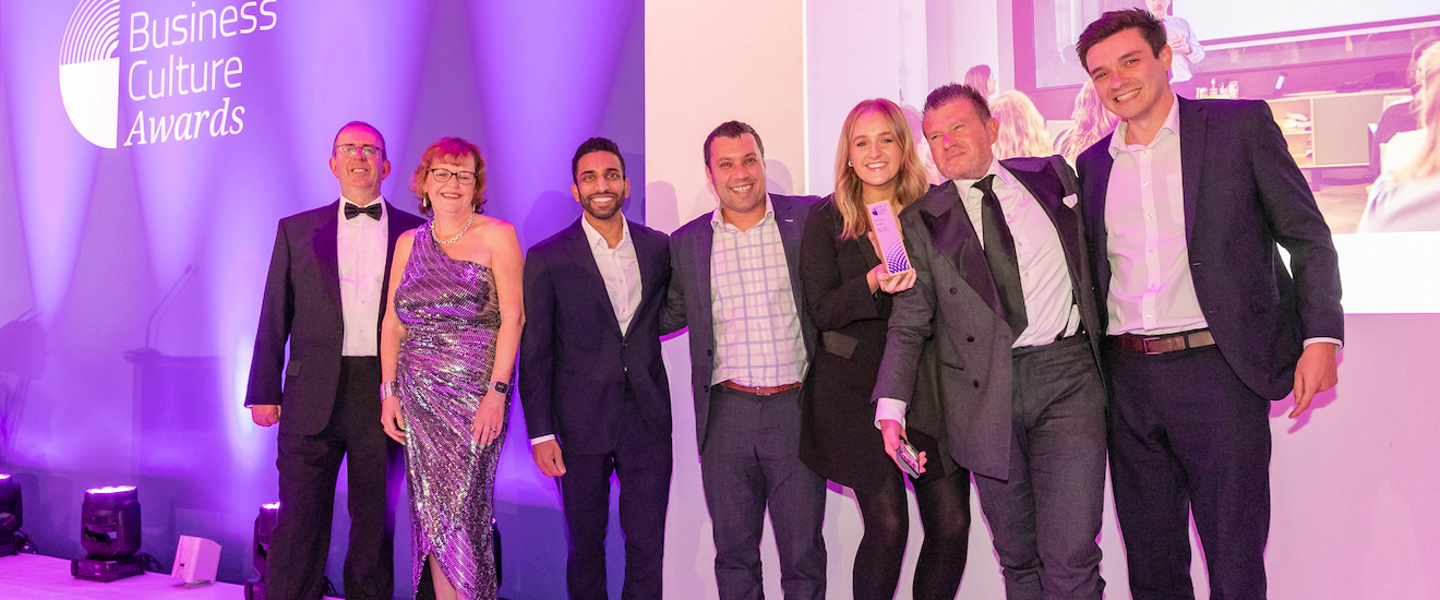 Colleagues smiling and accepting an award on stage at an award ceremony