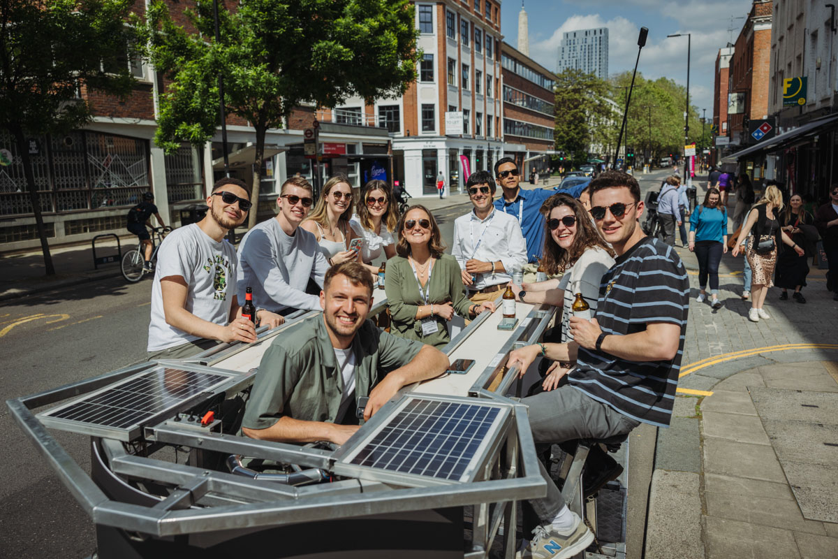 A group of people drinking a beer in London in the summer, smiling for a photograph.