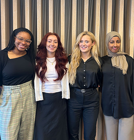 Four interior design interns stand in front of a wooden joinery wall in a London office