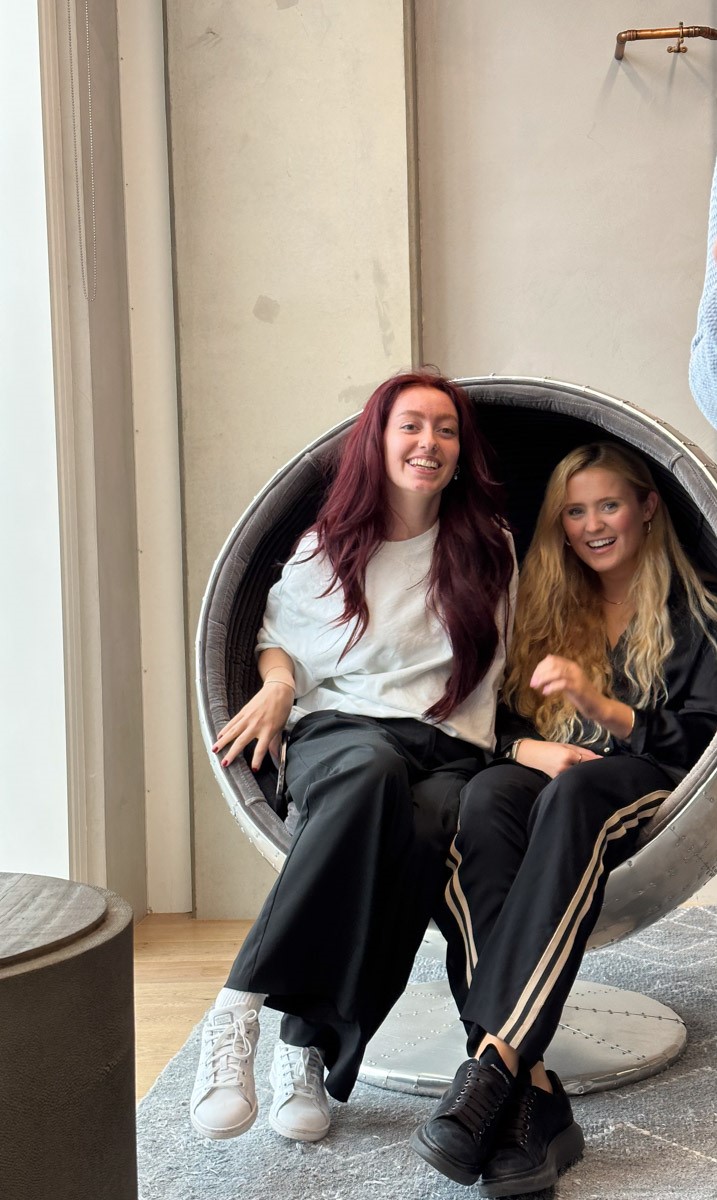 Two interior designs sit on a cool space ship chair laughing