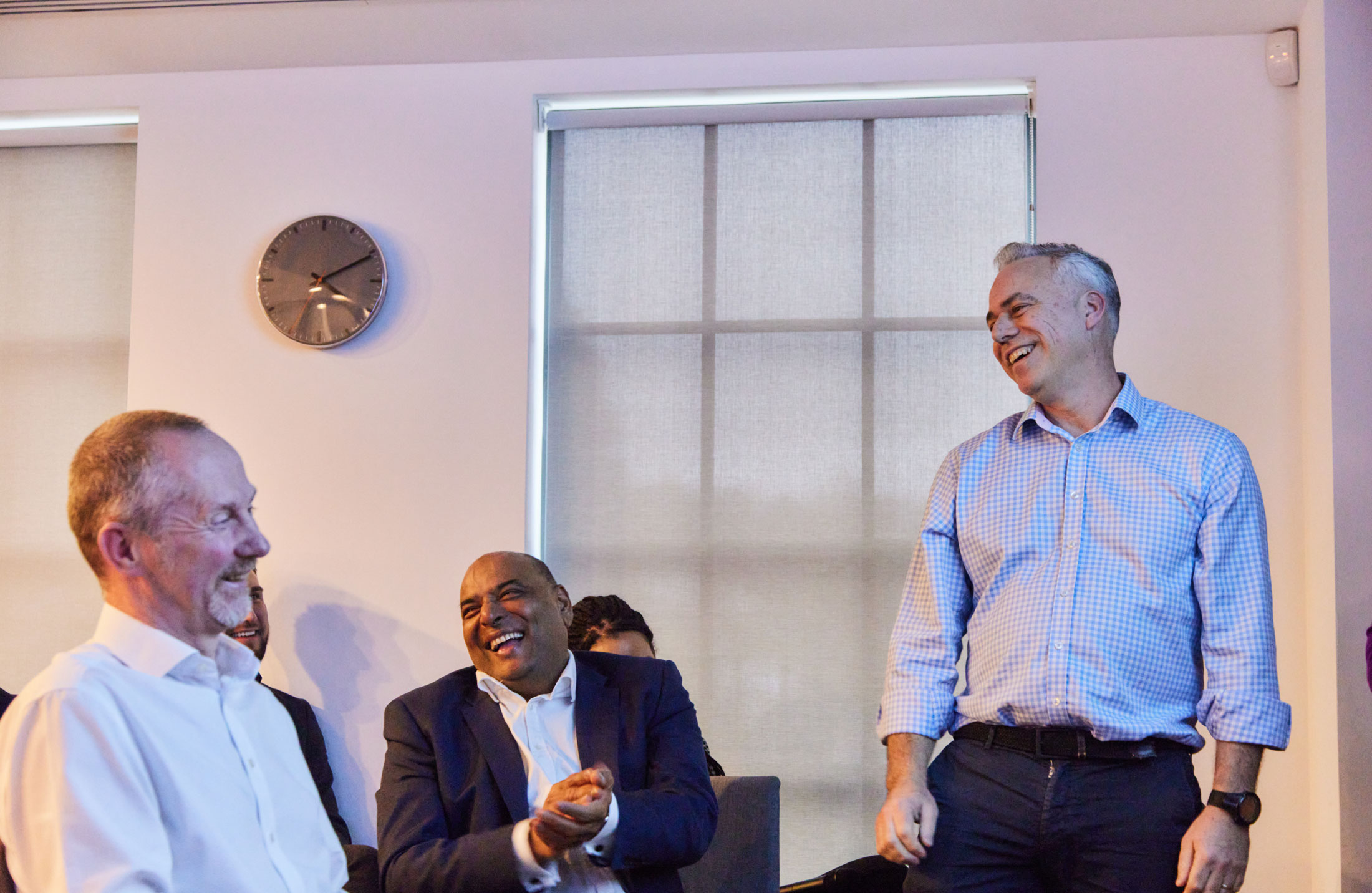 Three men laughing together in an office at a presentation.