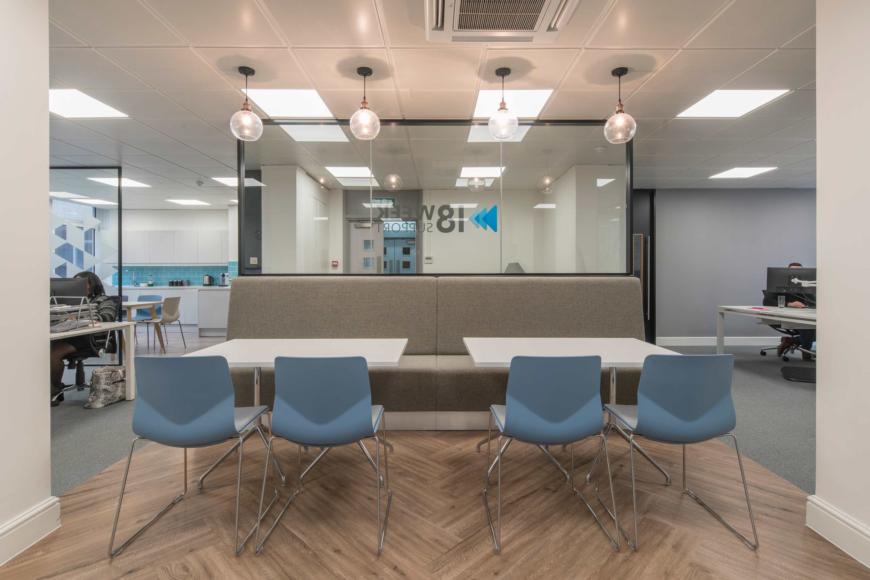 an open office with a grey booth and blue seats surrounding two white tables