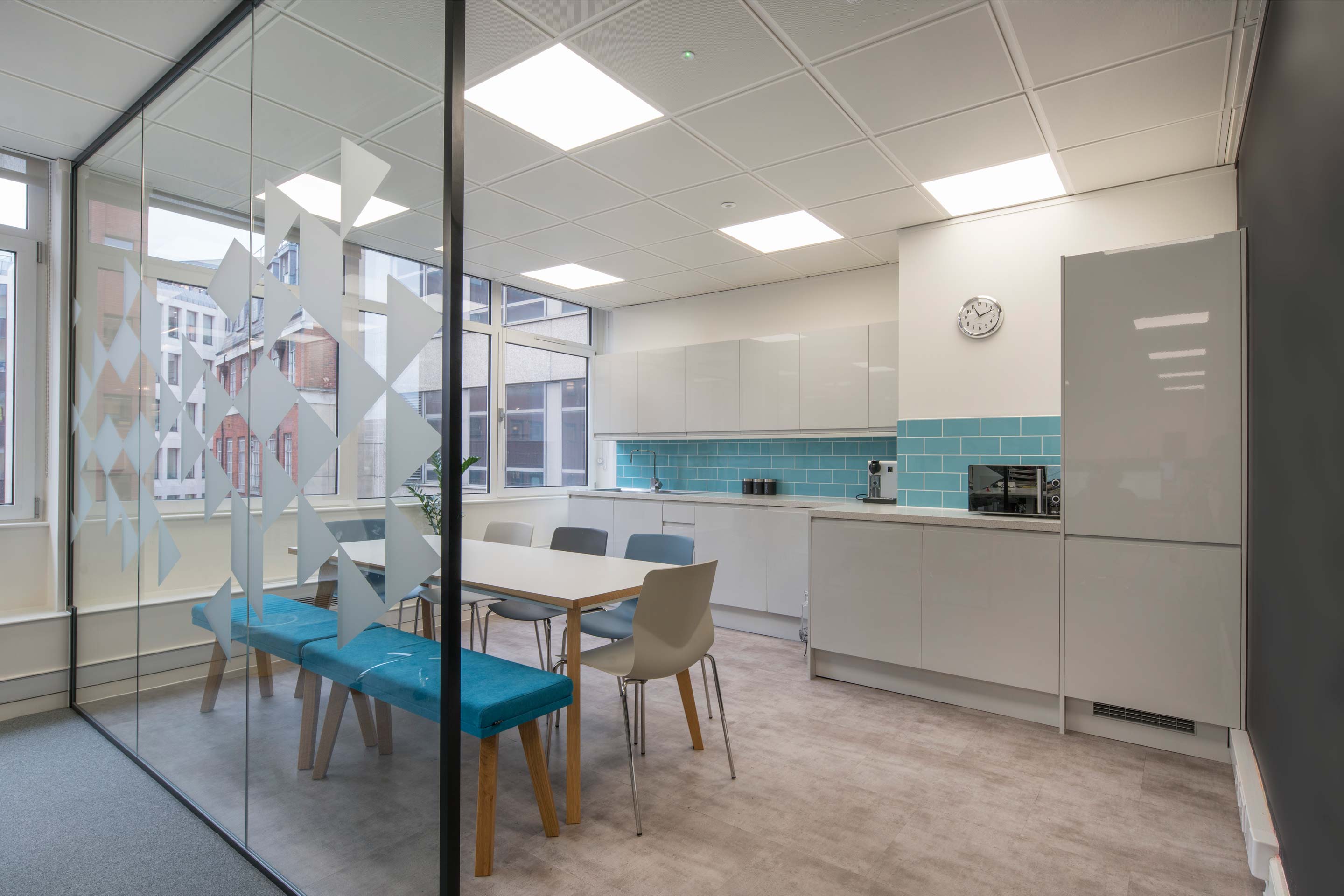 Grey kitchen with blue tiled backsplash and glass divider with a table and chairs