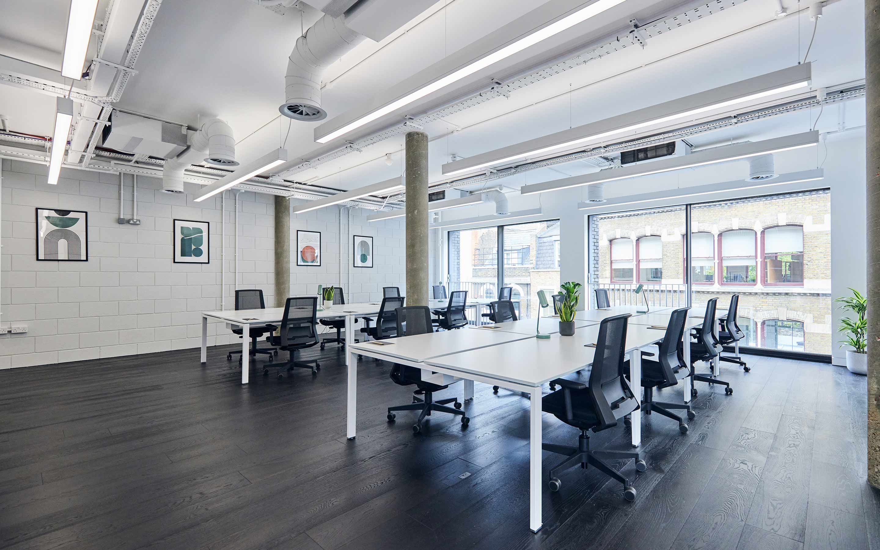 The image shows an open plan office, with artwork on the walls, linear ceiling lighting, and white walls