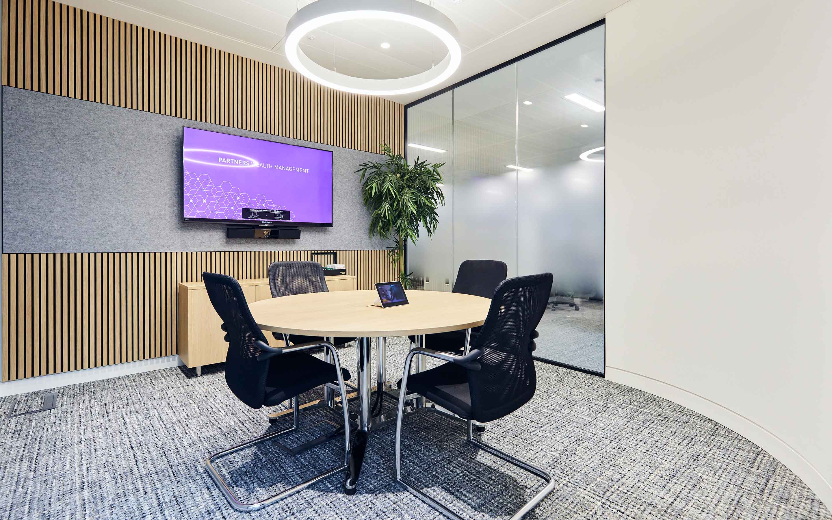 A meeting room with acoustic wall panelling, grey carpet, round meeting table and chairs, and a curved wall
