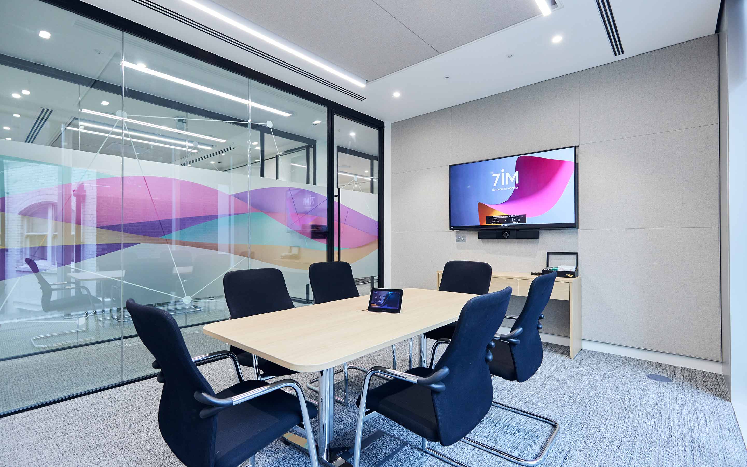The image shows a meeting room with acoustic panelling, and glass walls