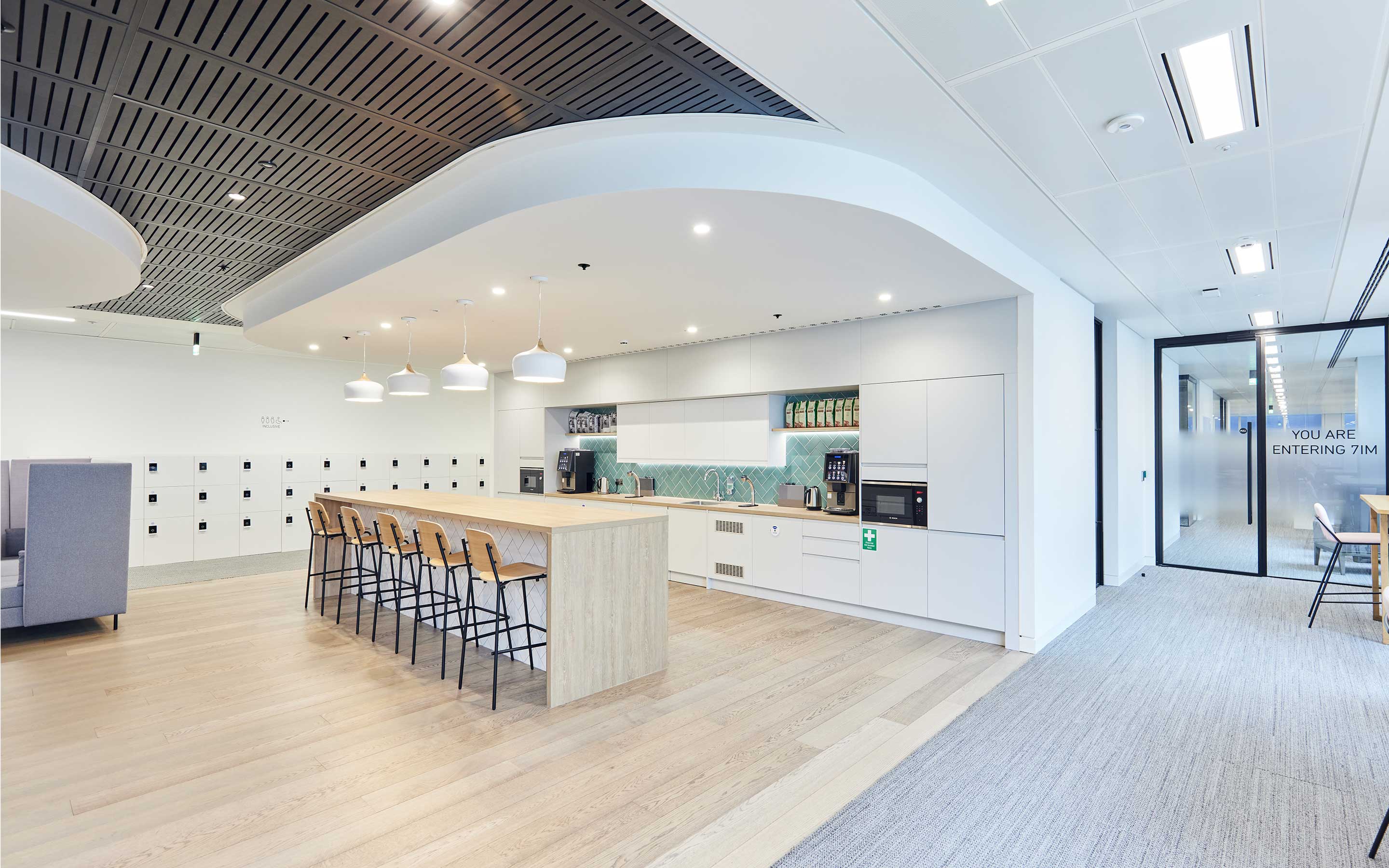 The image shows a bright office kitchen with pale wooden floors, white cabinets, and storage cabinets