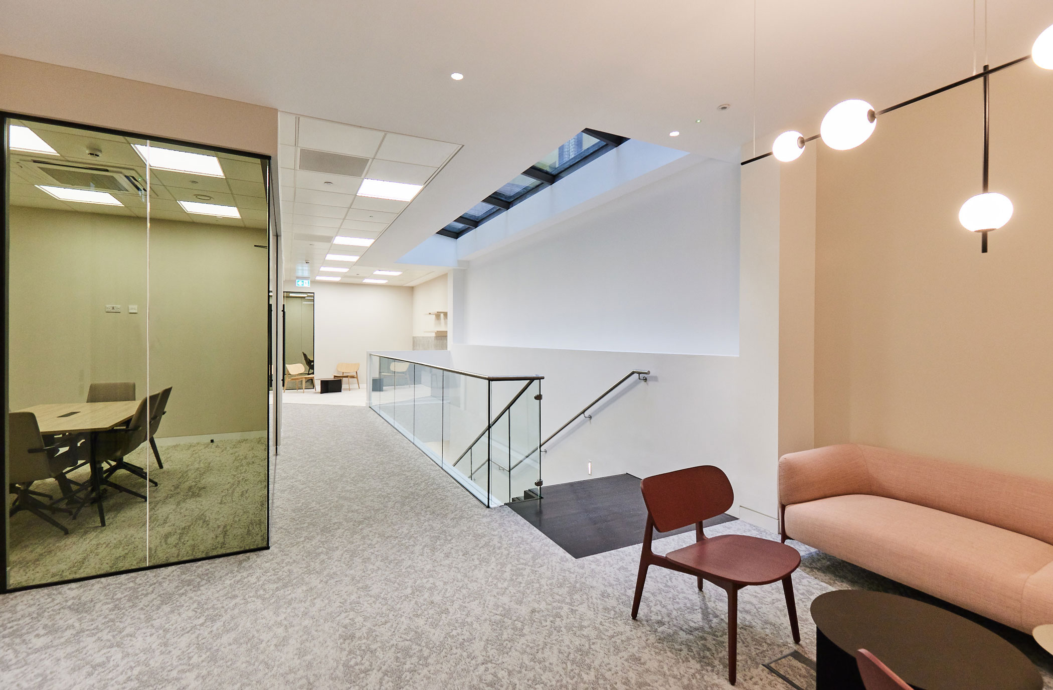 Feature lighting over soft seating and a pink upholstered sofa create a welcoming reception area in a new office design