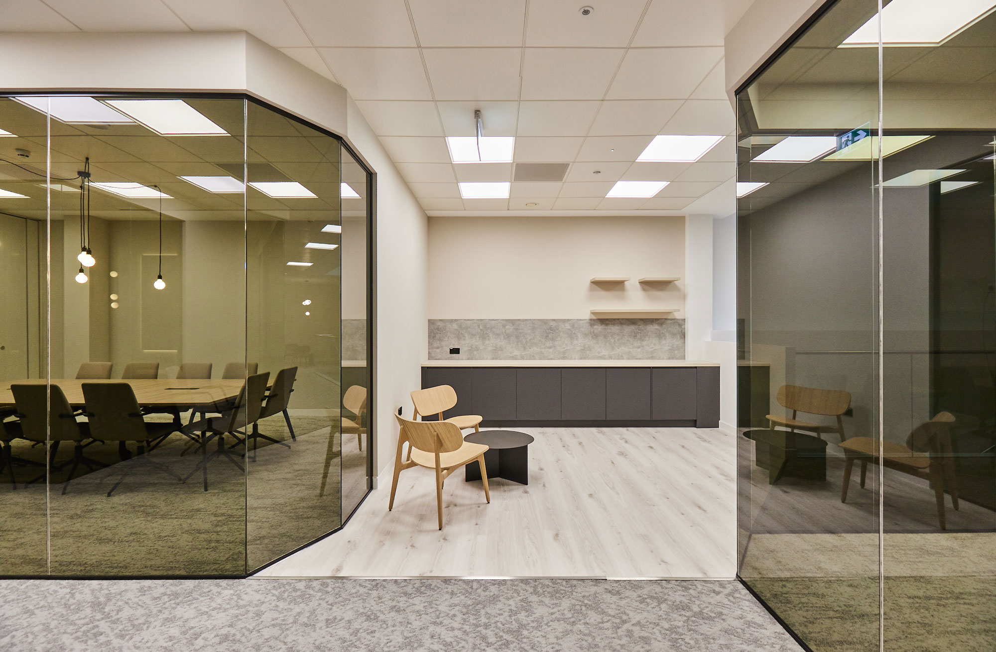 Glass walled meeting rooms feed off a small social space and tea point, complete with minimalistic wooden chairs and a coffee table