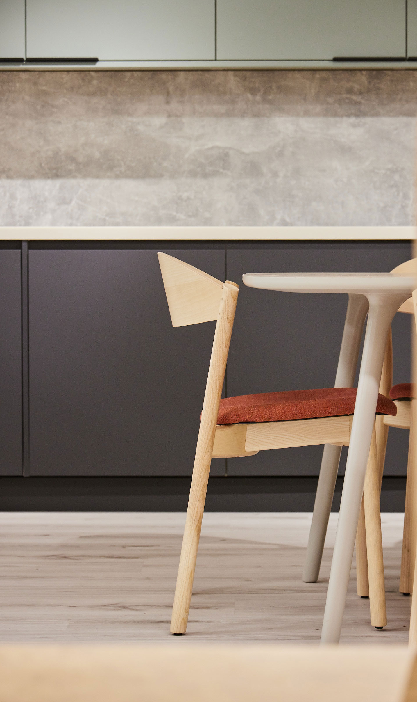 Minimalistic wooden chair with soft orange seat pad in a kitchen with marble backsplash tiles and matte grey counters