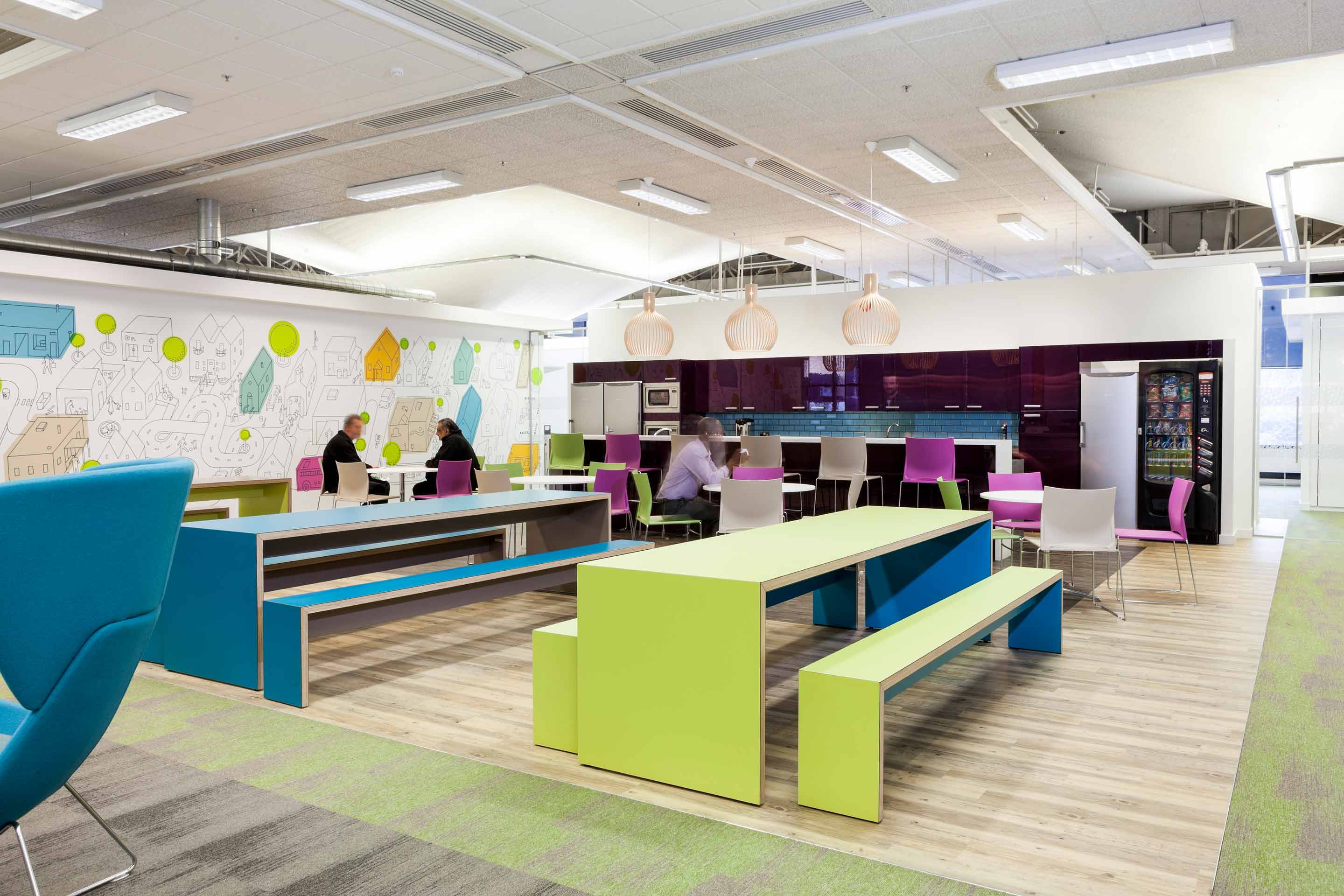 A purple kitchen with people sitting at multicoloured circle tables and rectangle benches.