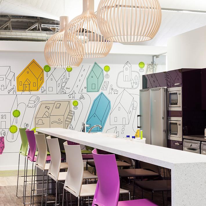 Low-hanging peach slatted lamp shades with purple, white, and green chairs at a white kitchen island