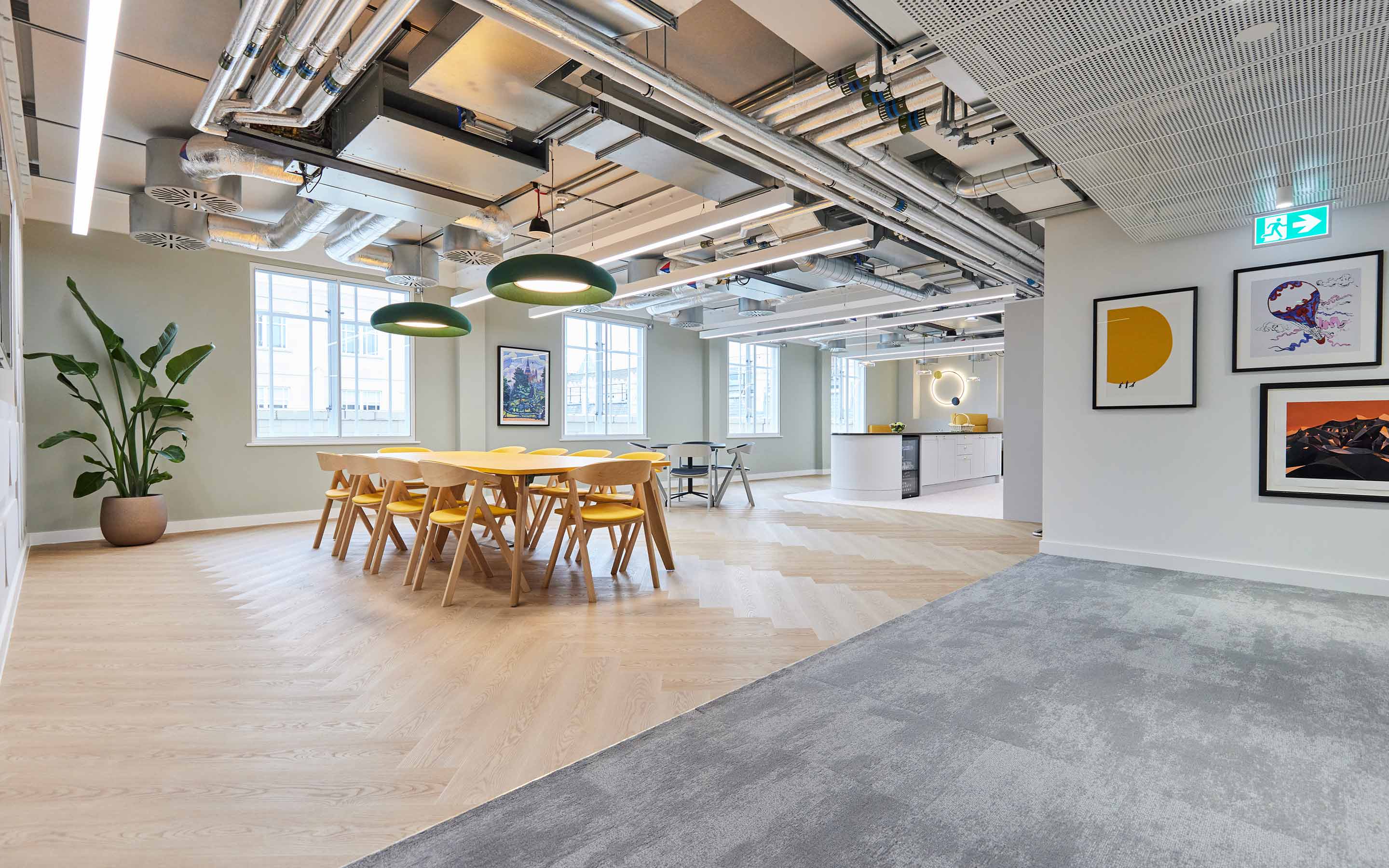 An office kitchen, complete with artwork, kitchen table and chairs, pendant lighting, and potted plants