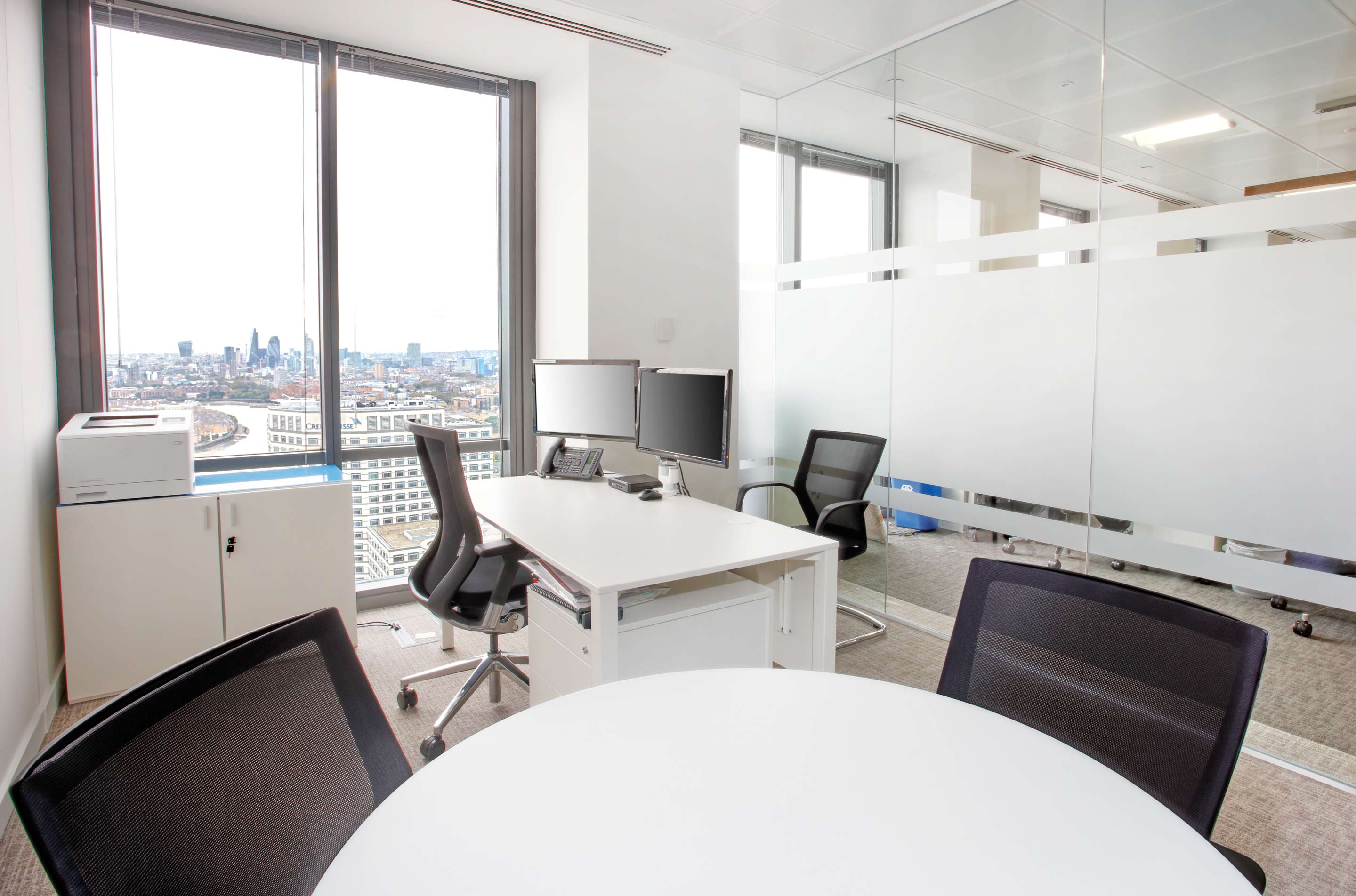 two white desks in a small white office with natural light