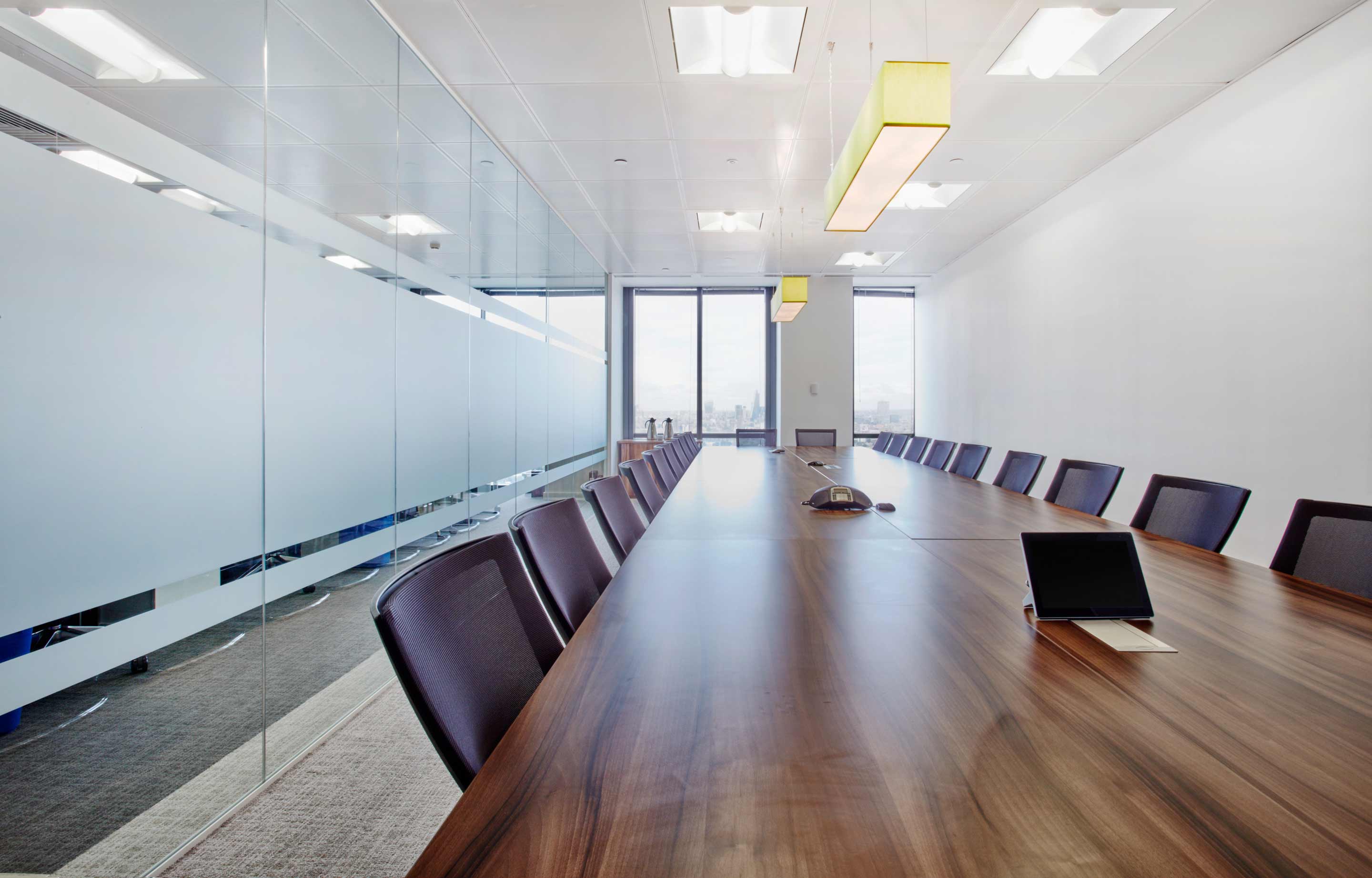 A long dark wooden boardroom table to the left of a glass wall