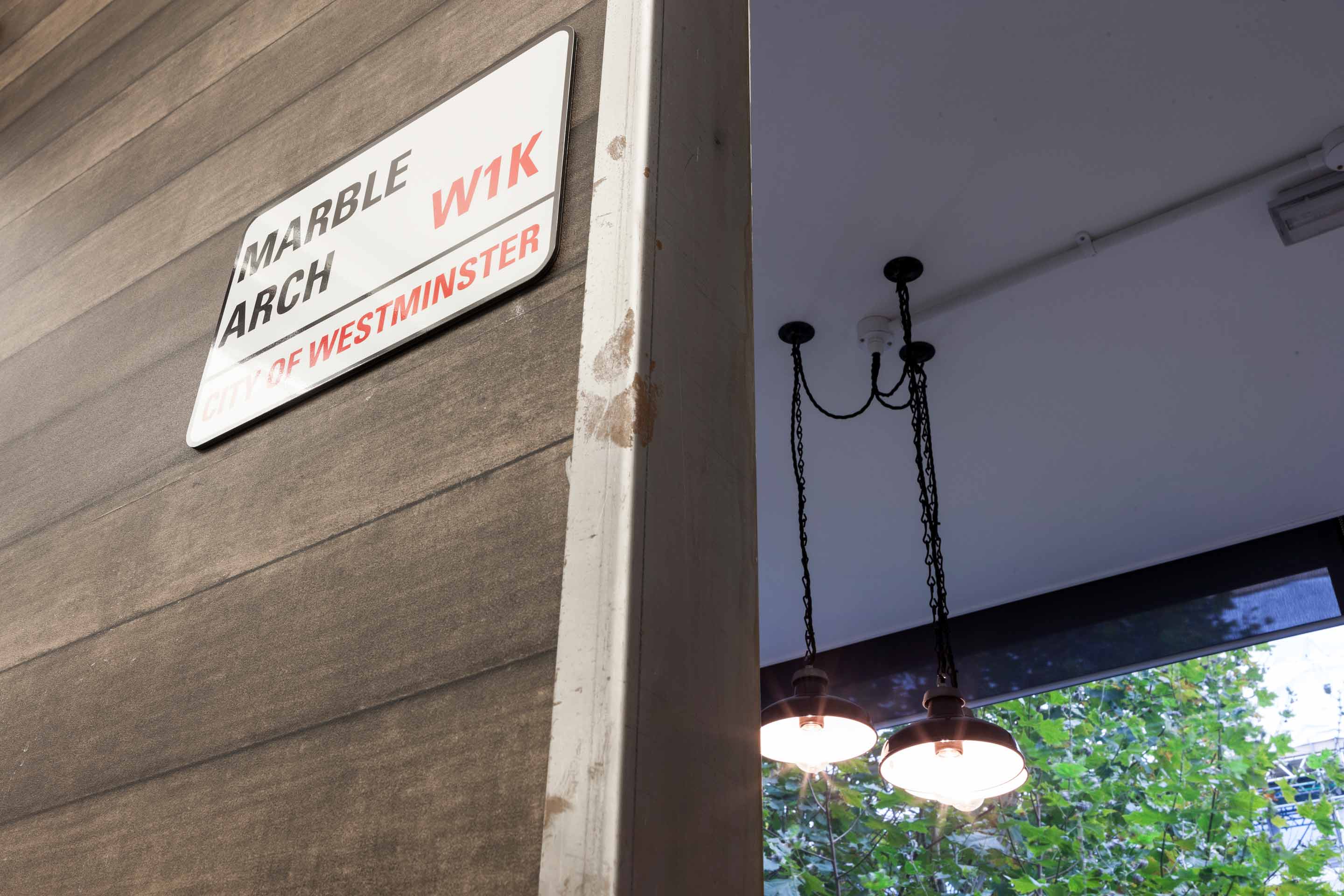 A white street sign fixed to a dark wooden finished wall with low handing mental lighting