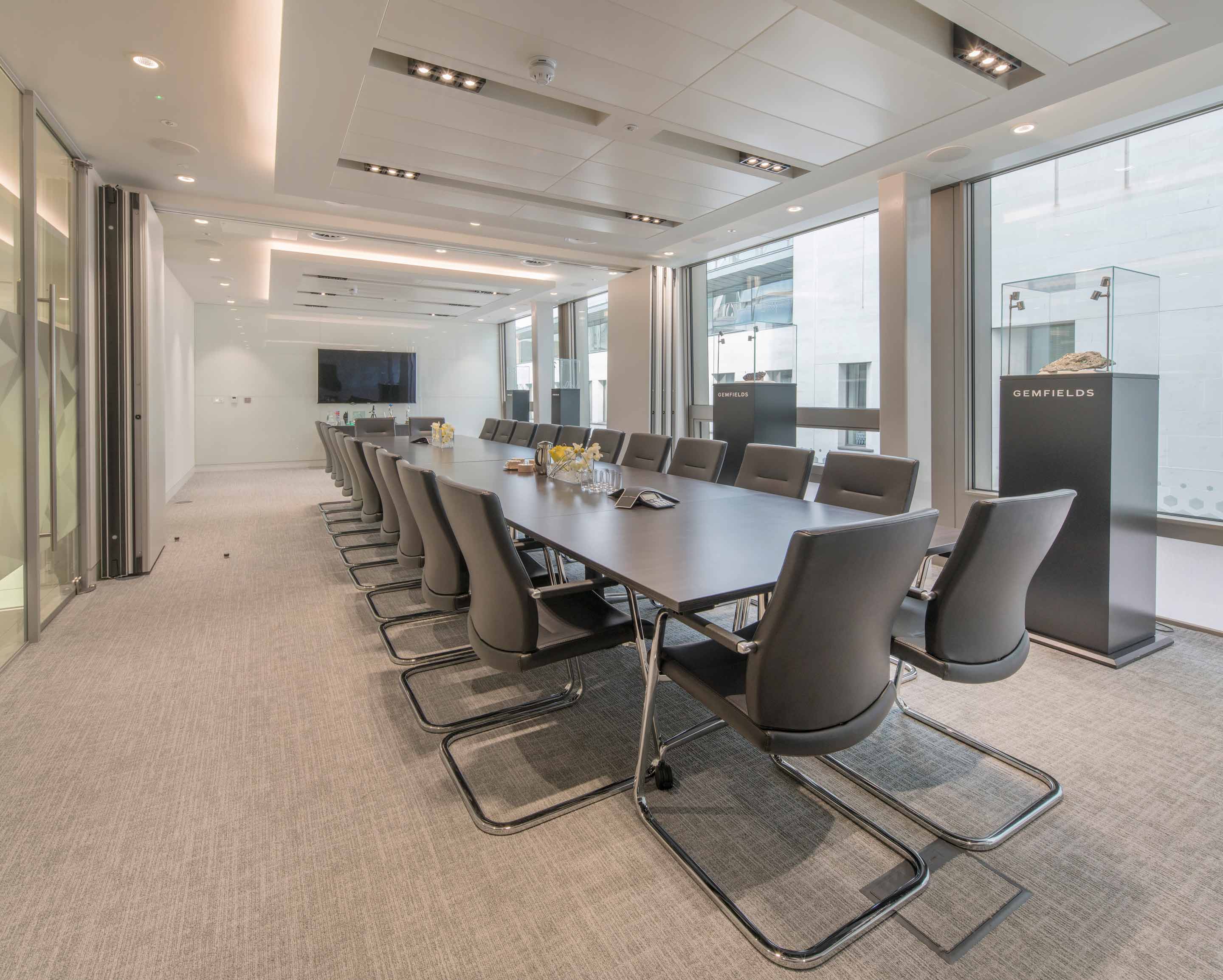 Meeting room with a grey rectangle table with glass encased displays along the outside wall