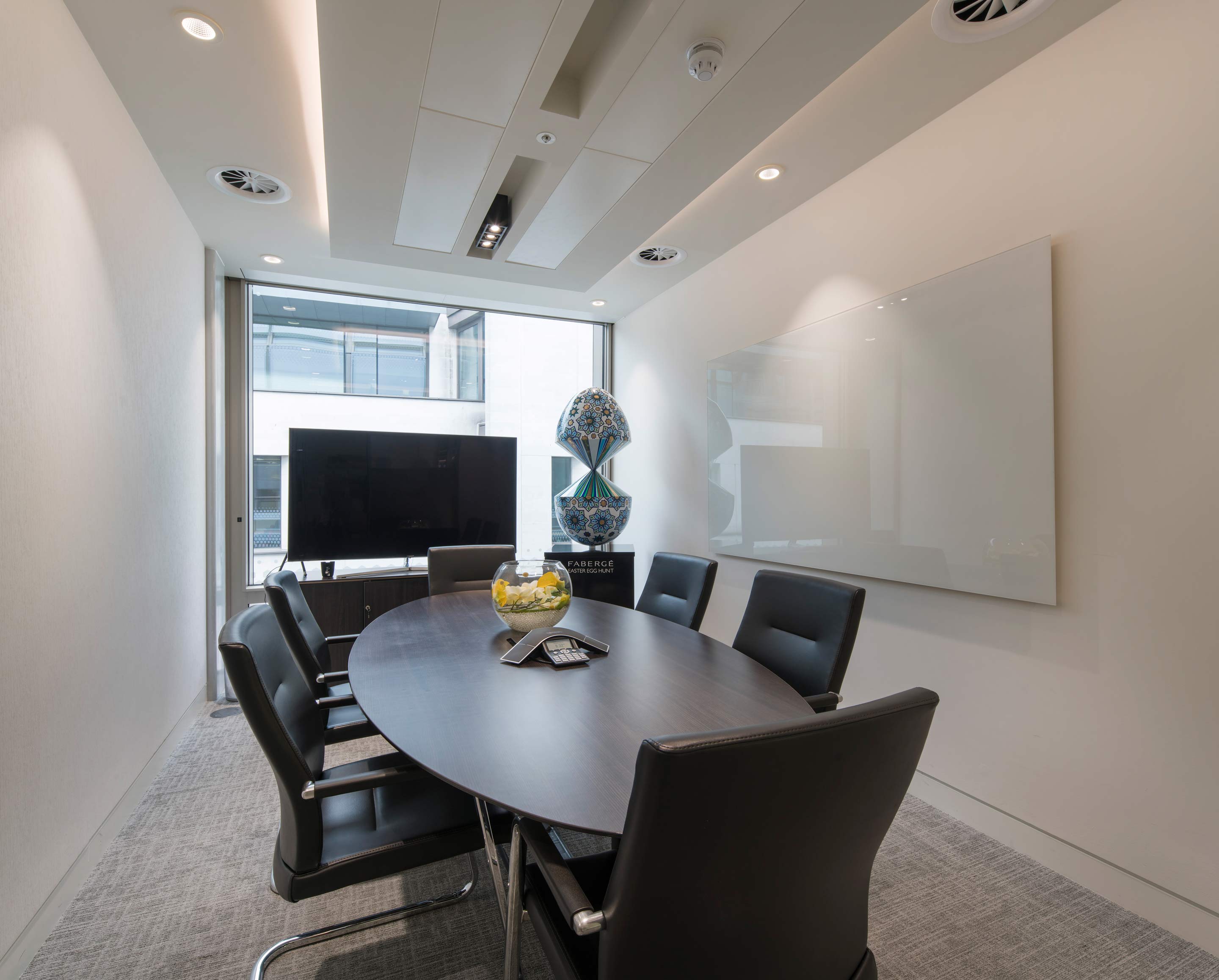 Small meeting room with an oval table set in the middle and a TV on the outside wall next to a fabricia