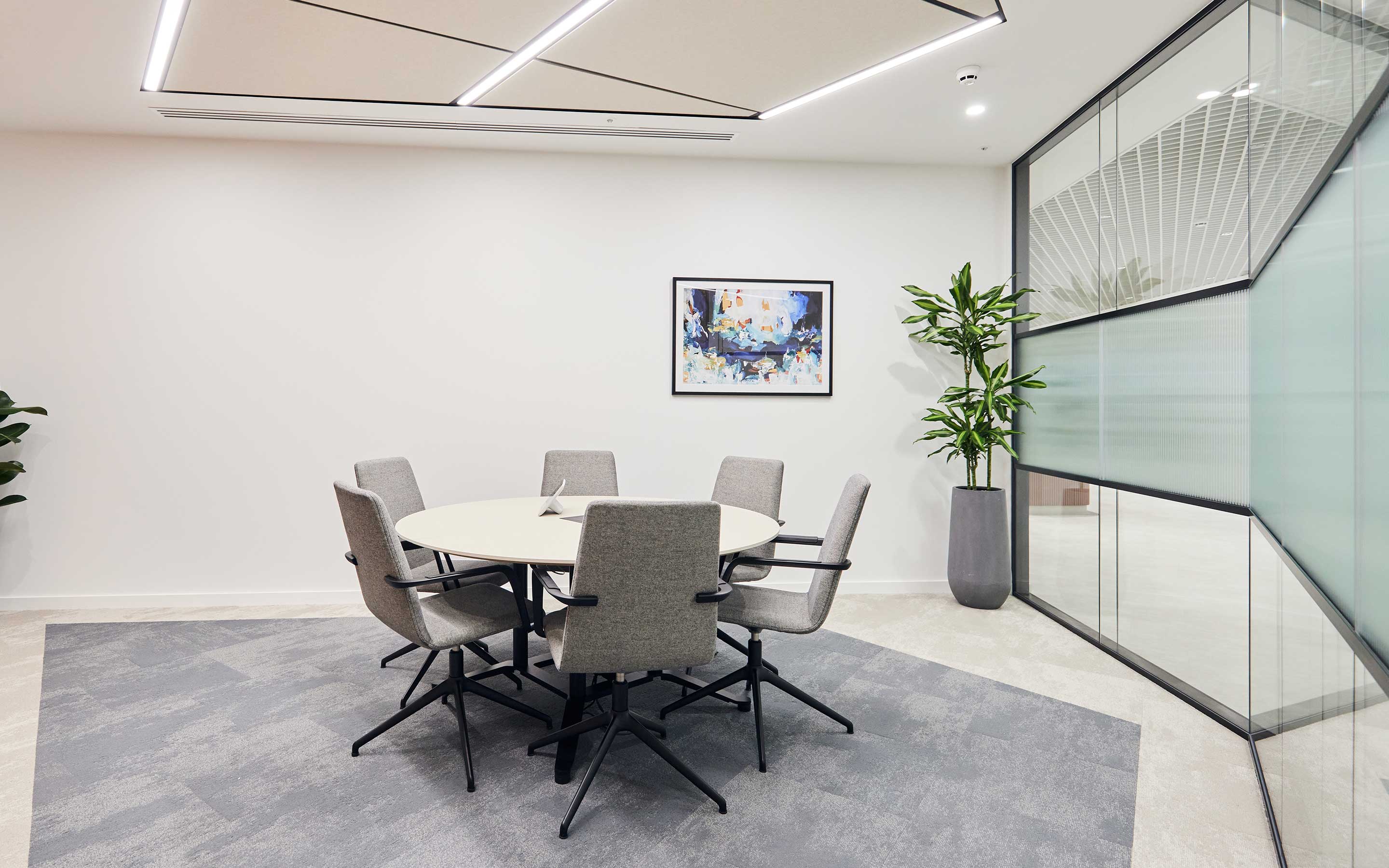 A modern office meeting room with glass walls, a round meeting table and chairs, and lovely artwork on the wall