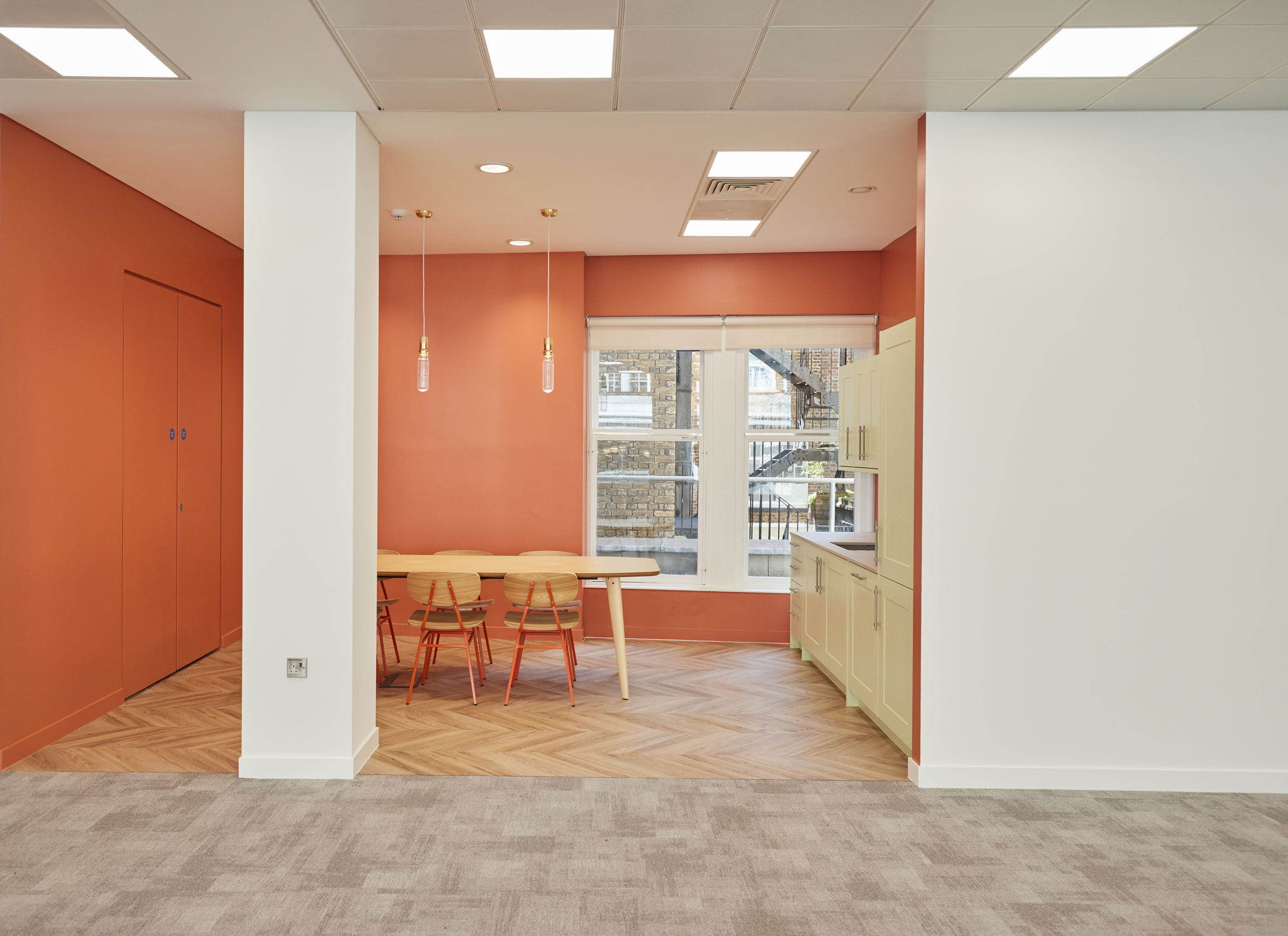 Tea point and social space with salmon pink wallpaper and wooden flooring