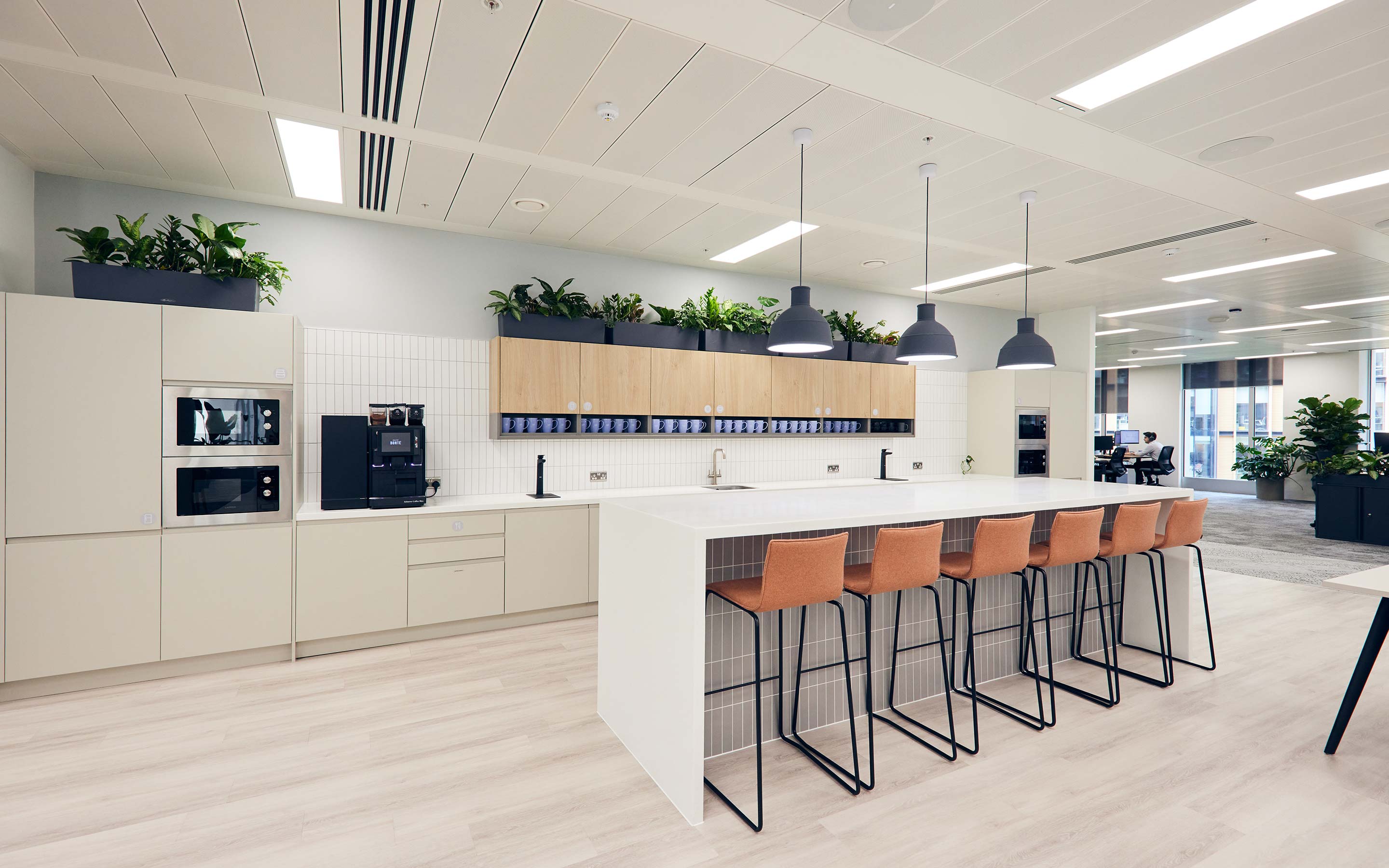 An office teapoint features kitchen facilities complete with salmon pink high breakfast stools, and views of the open plan office