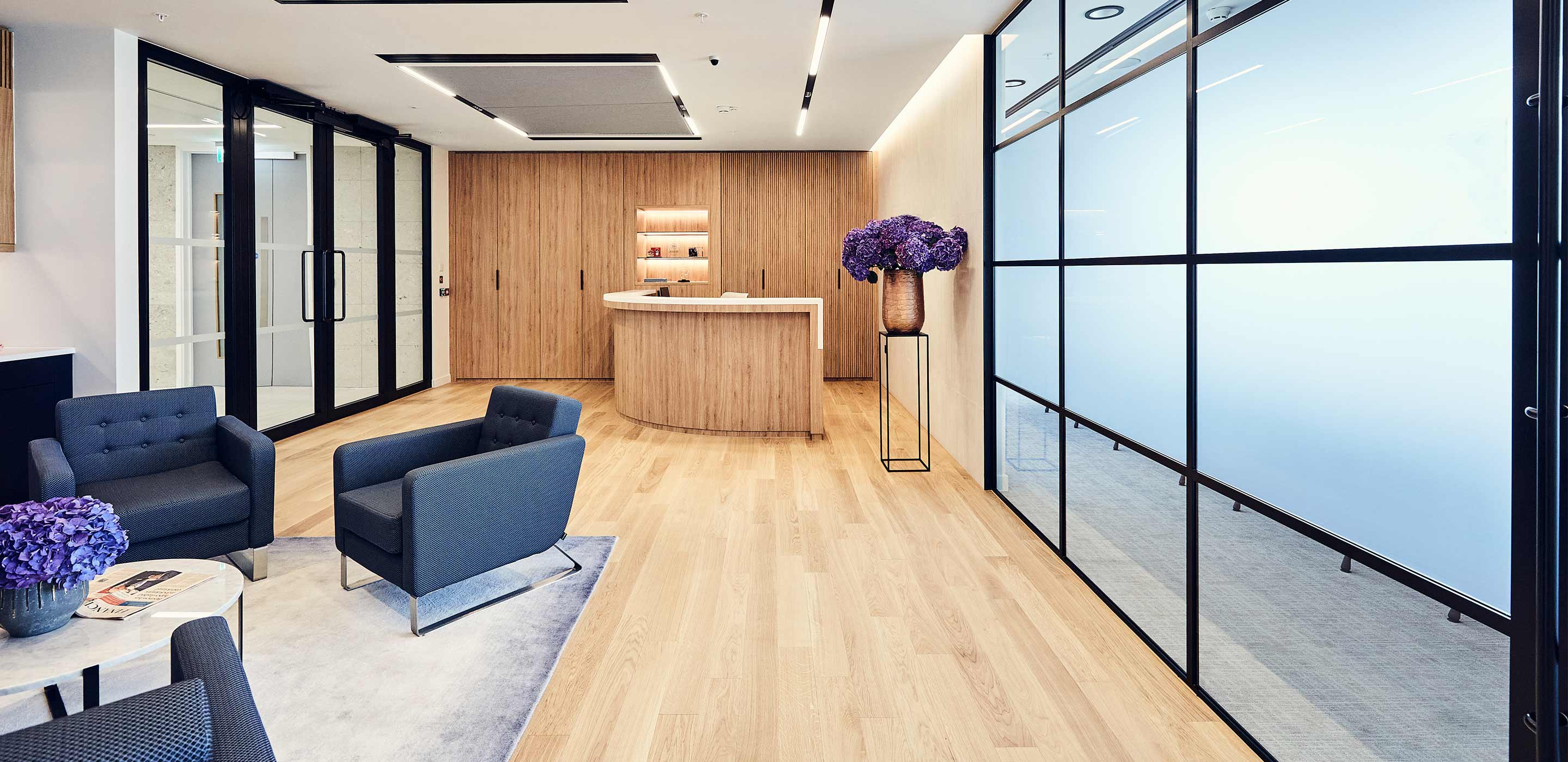 Workplace reception with curved, timber desk and blue armchairs