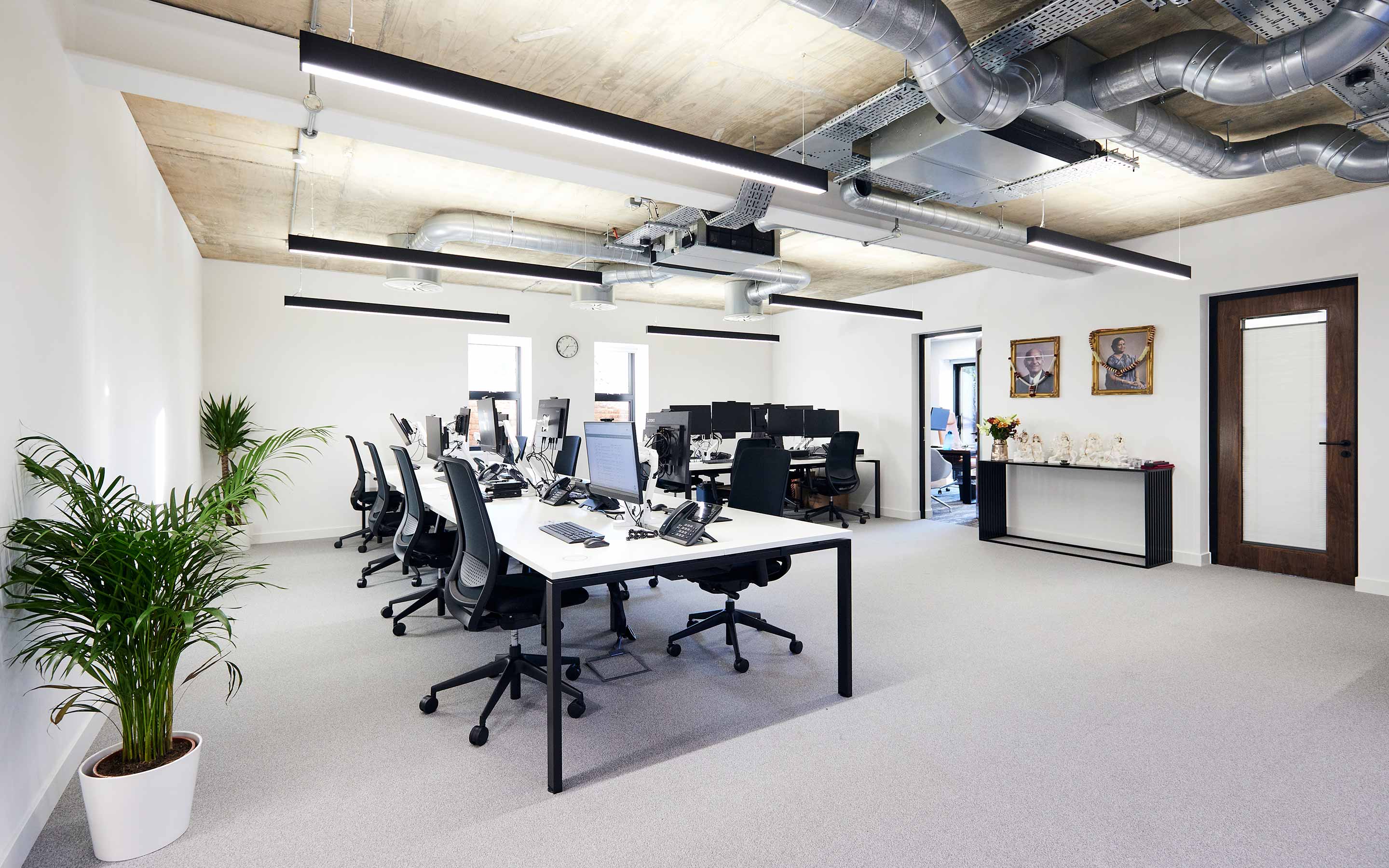 A spacious office with desks and computers, showcasing modern workplace design in a large room with exposed mechanical and electrical services and a bright aesthetic