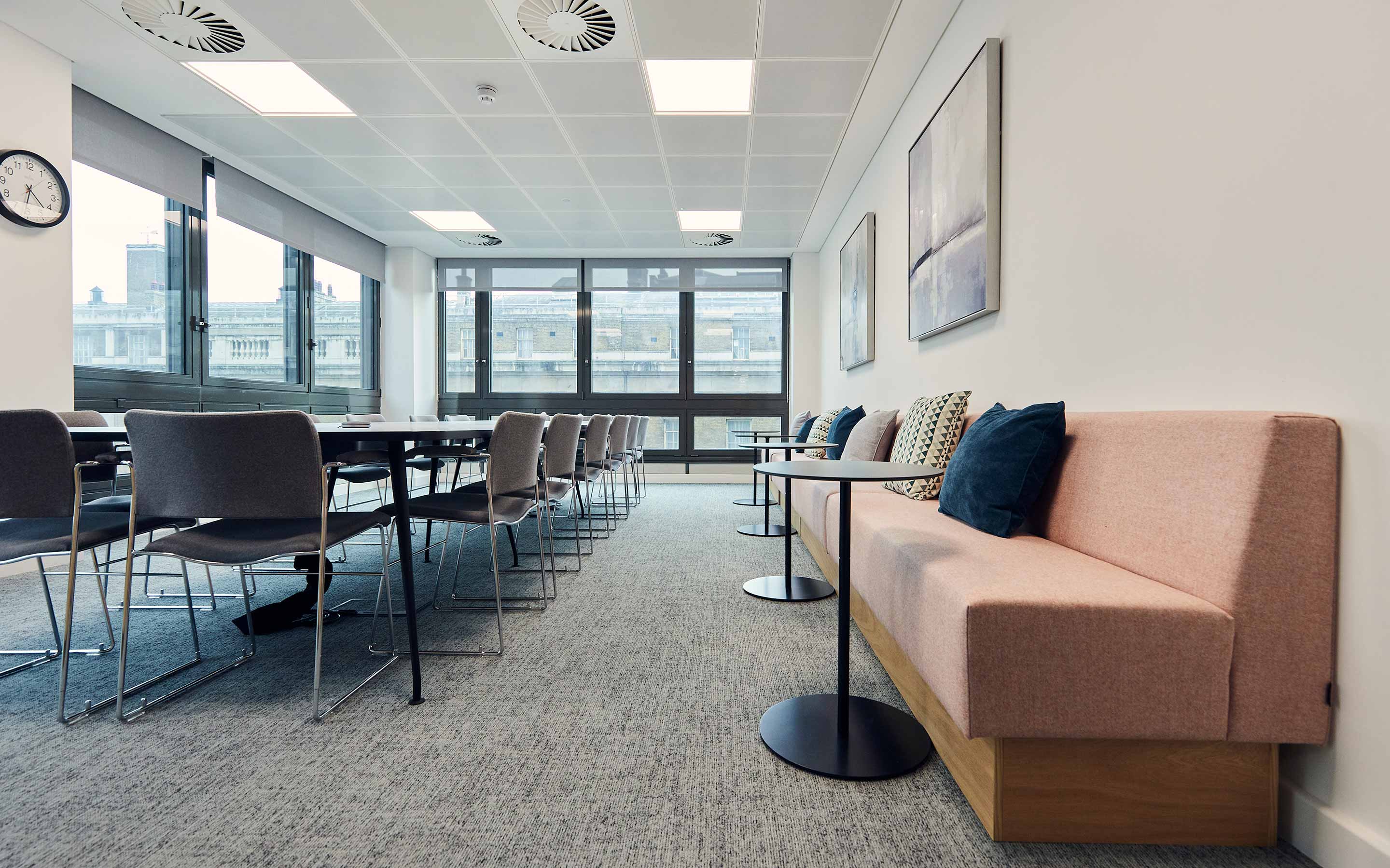 The boardroom of an office includes a large boardroom table and chairs, and soft pink banquette seating along the wall