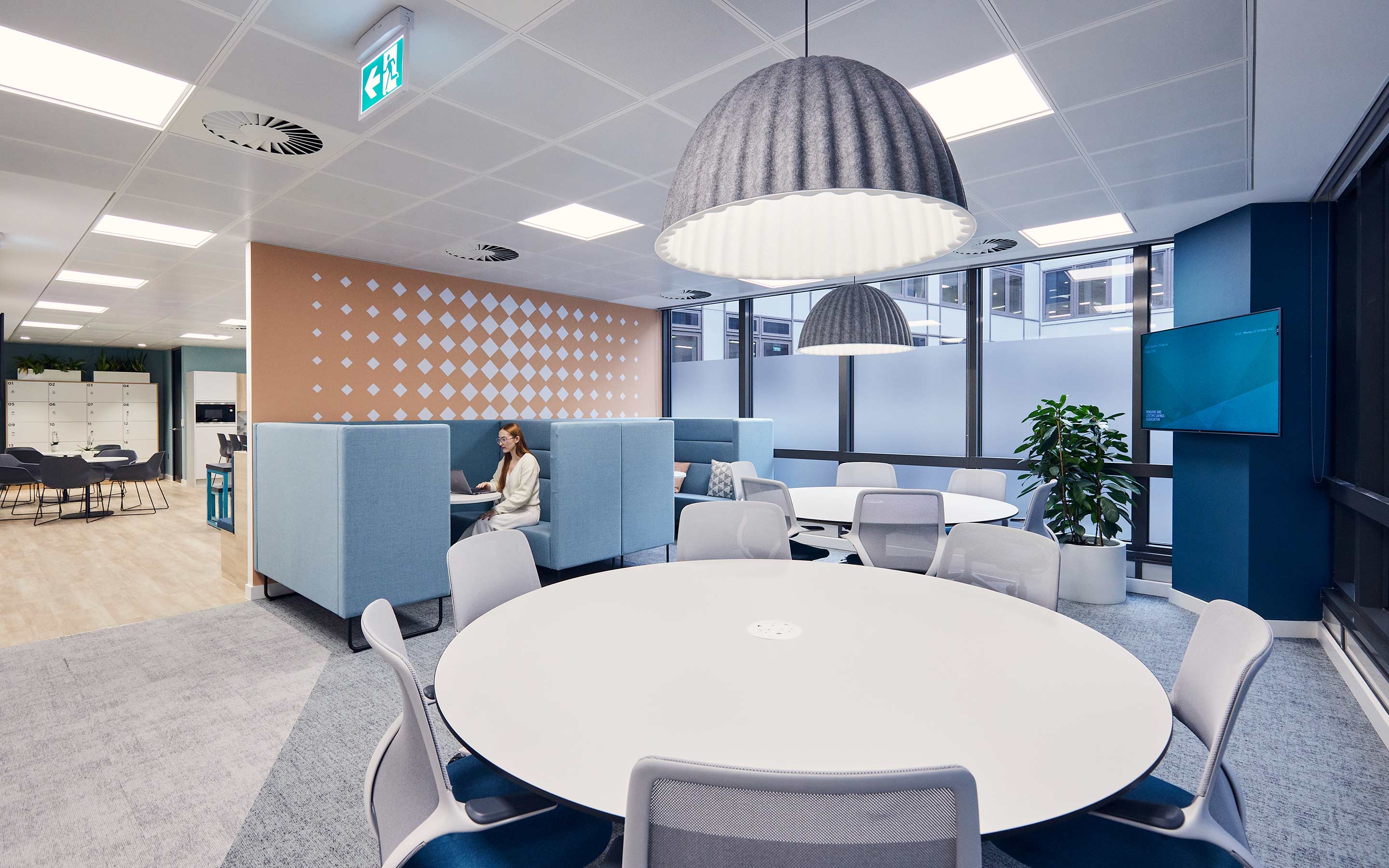 A breakout space features large dome pendant lighting, collaboration round tables, meeting booths, and a blue aesthetic