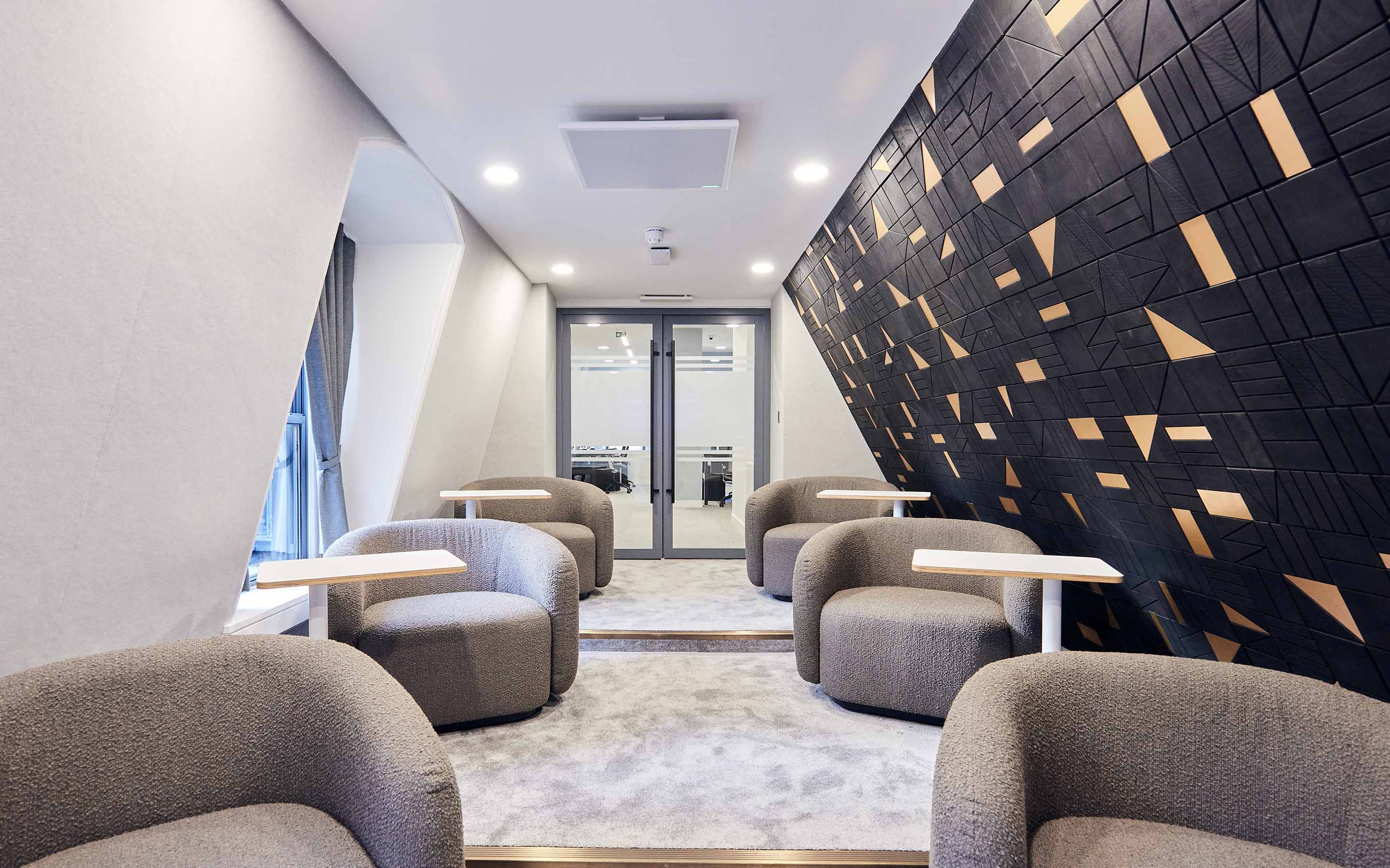 A well-designed office interior with comfortable chairs and tables, incorporating modern workplace aesthetics and a distinctive black wooden joinery wall