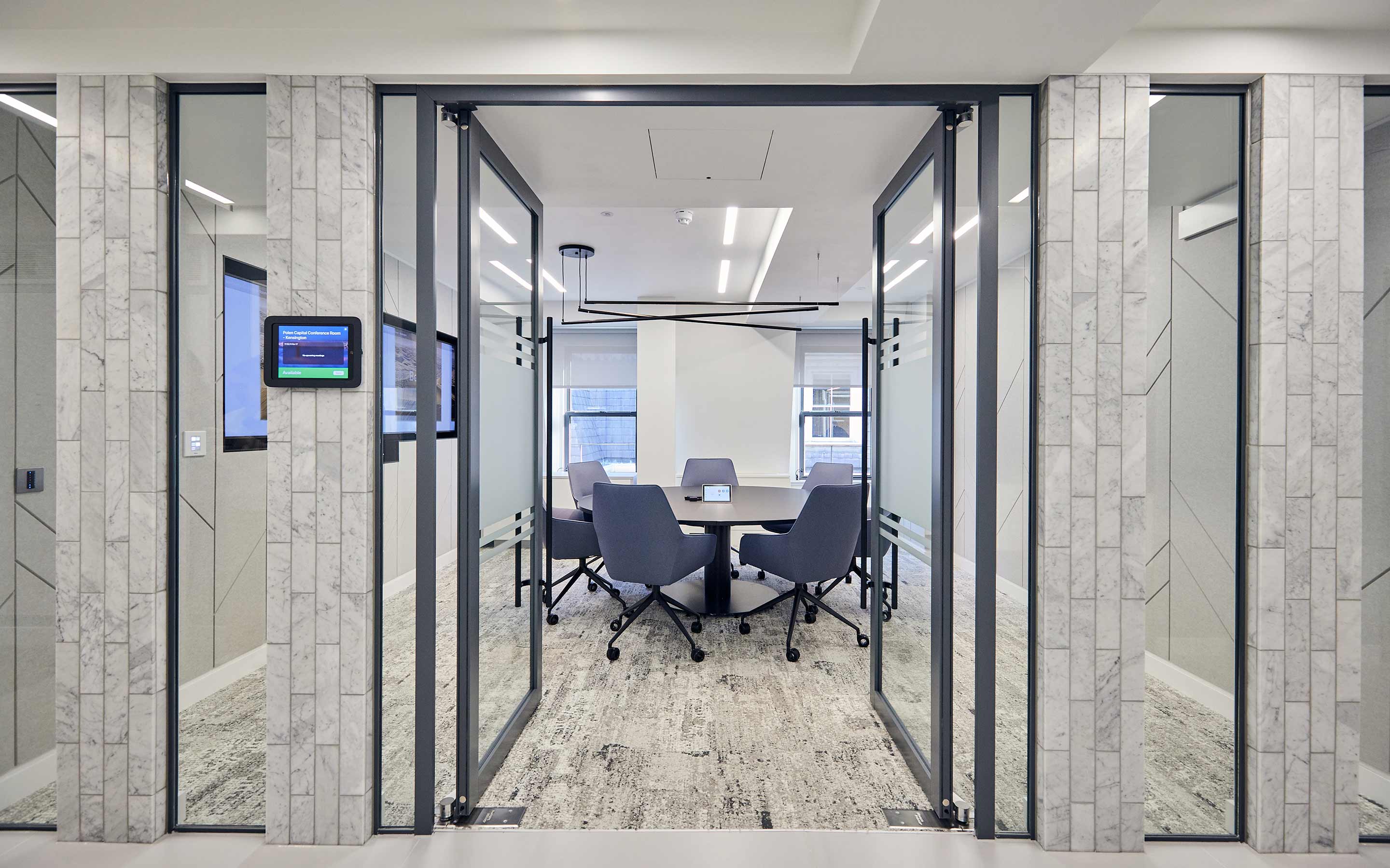 A well-lit conference room adorned with glass walls, blue chairs, and a stylish round table, reflecting a thoughtfully designed workplace for productive meetings