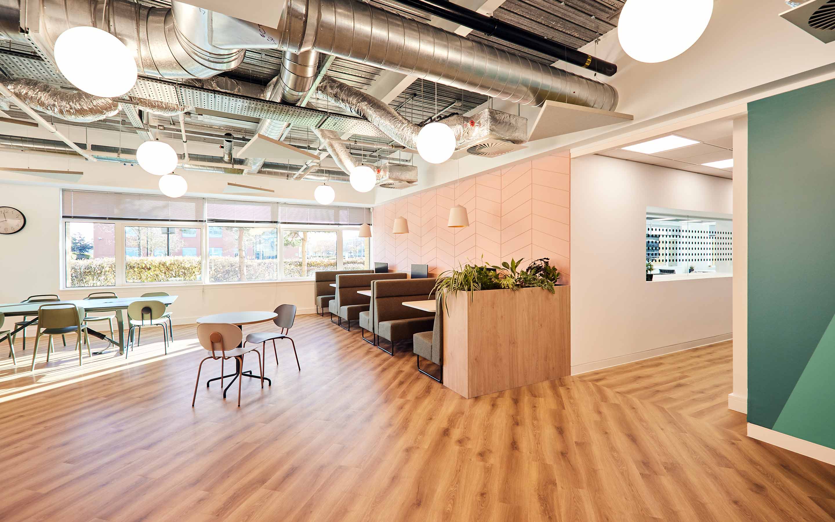A professionally designed office space featuring wooden floors, breakout booth seating and a soft pink joinery walls, creating a vibrant and inviting atmosphere