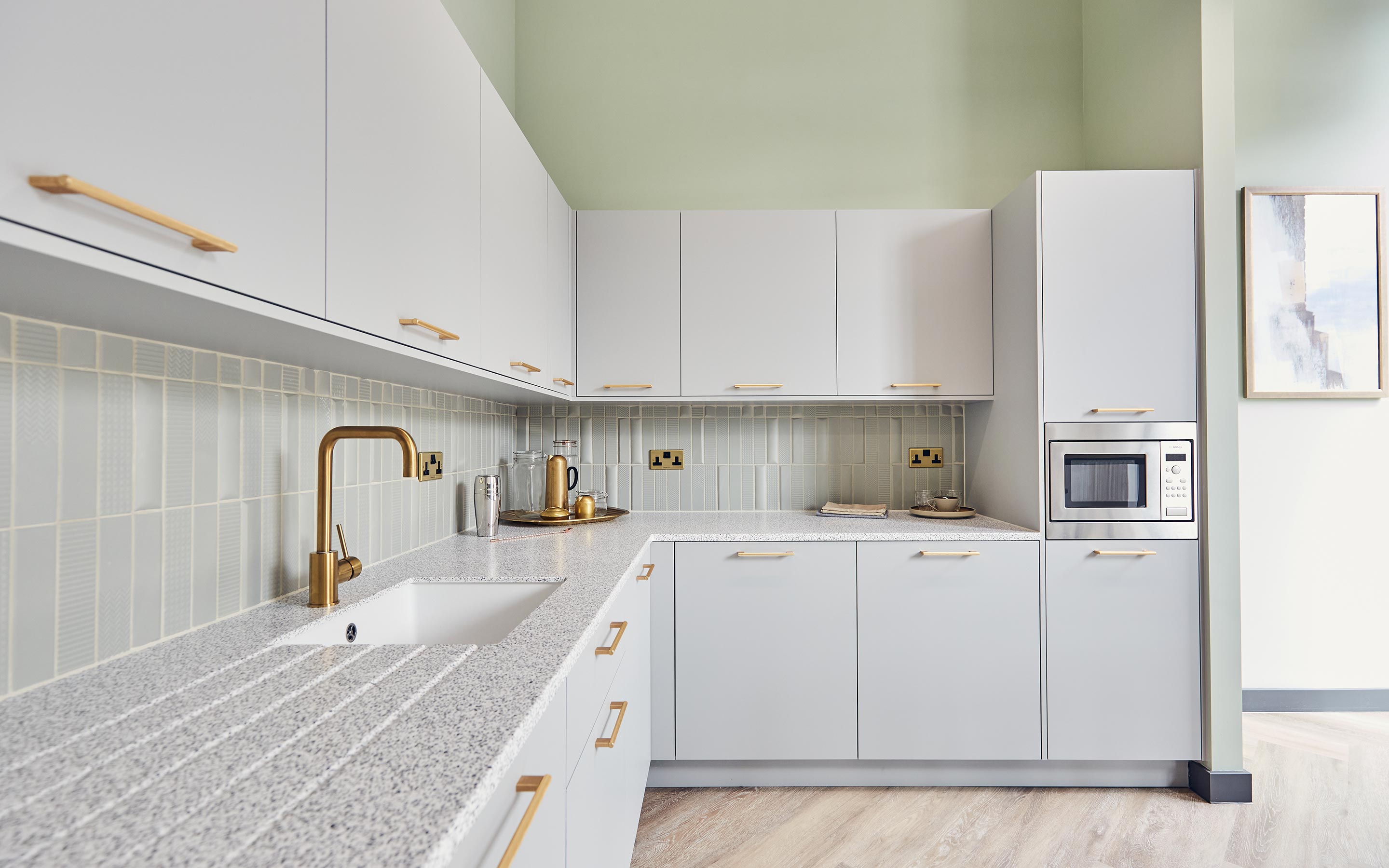 The image shows a kitchen with pale blue cabinets, gold fixings, and serene artwork