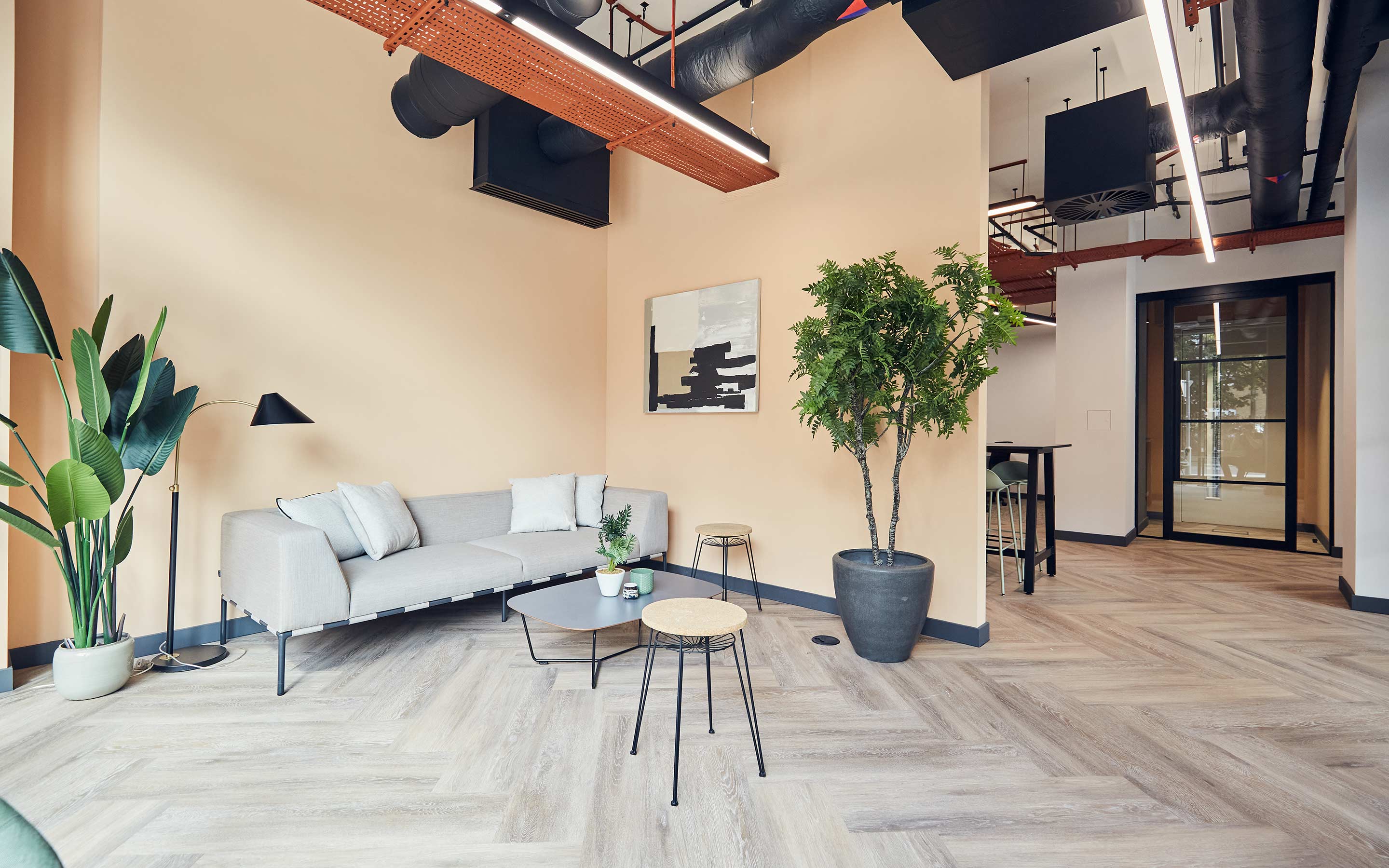The image shows an arrival area in a contemporary office, with soft furniture, wooden flooring and indoor planting