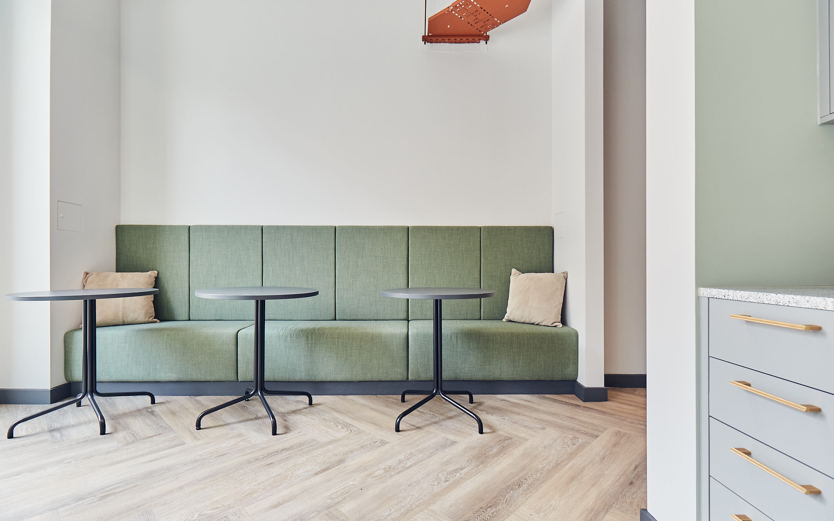 The image shows soft green banquette seating and laptop tables in an office tea point