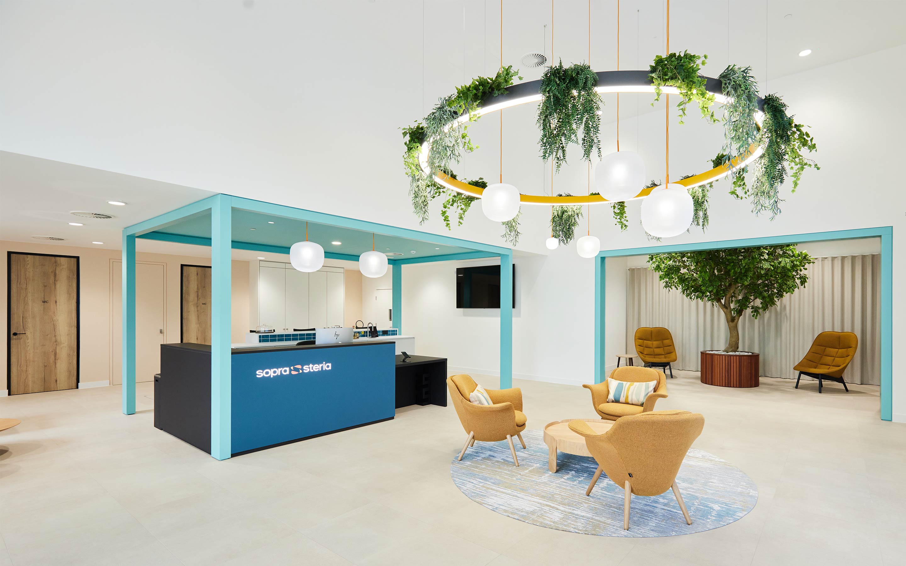 A large blue reception desk looks over a waiting area with soft seating and indoor planting