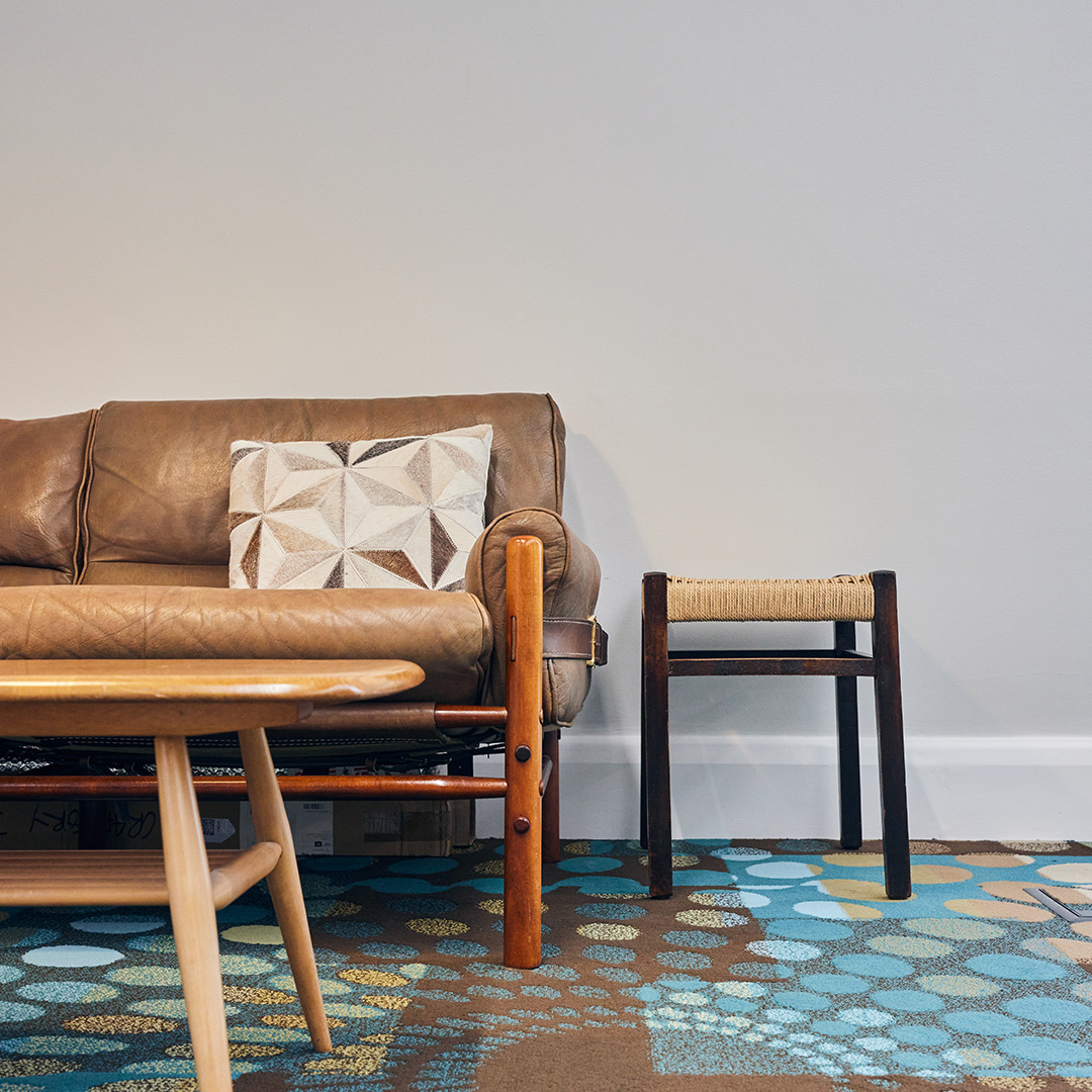 The image shows a vintage leather sofa and wicker stool in an office