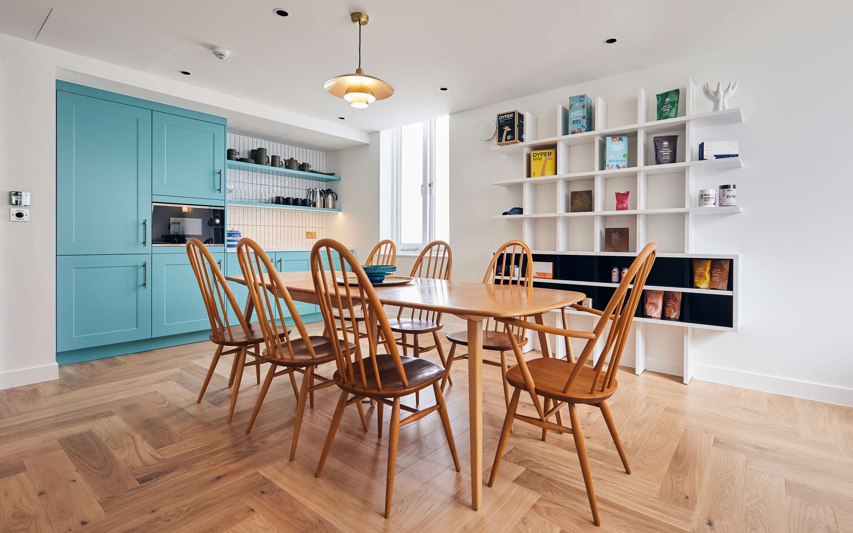 The image shows a wooden kitchen table and chairs, duck egg blue cabinets and shelving units filled with crockery