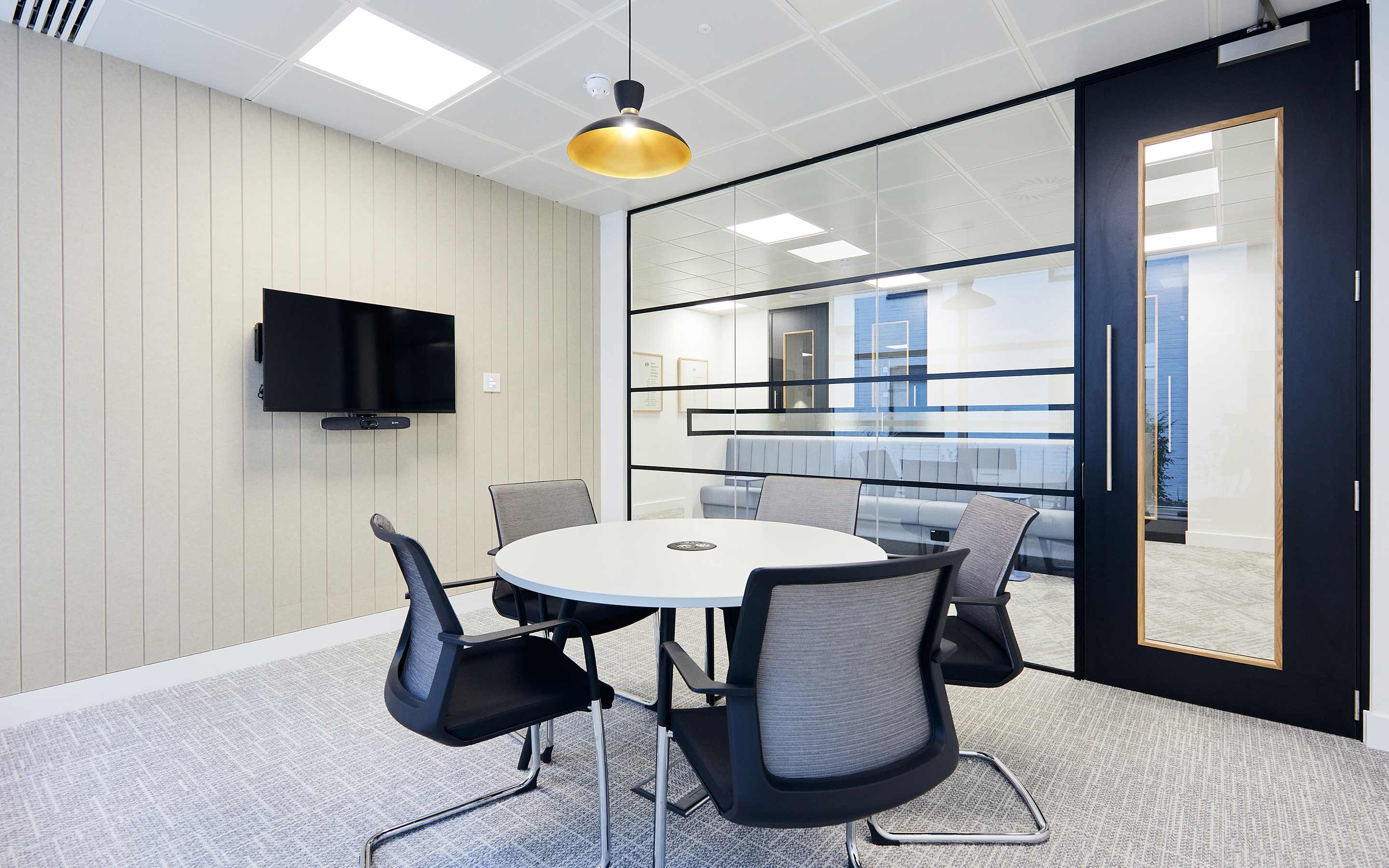 A meeting room in a modern office, with chairs and a round table, and glass walls