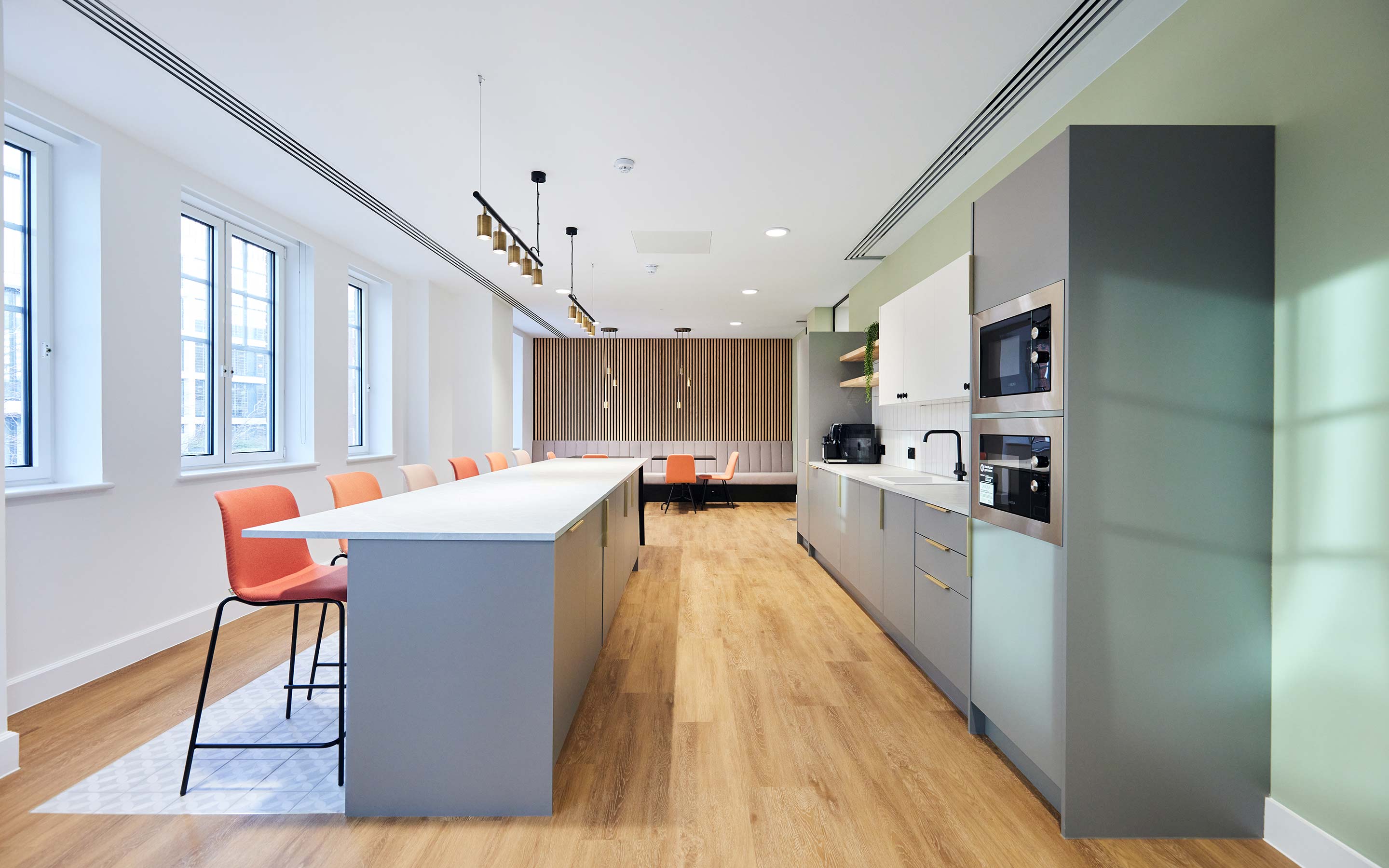 A contemporary kitchen in a London office with timber flooring, and soft grey kitchen cabinets