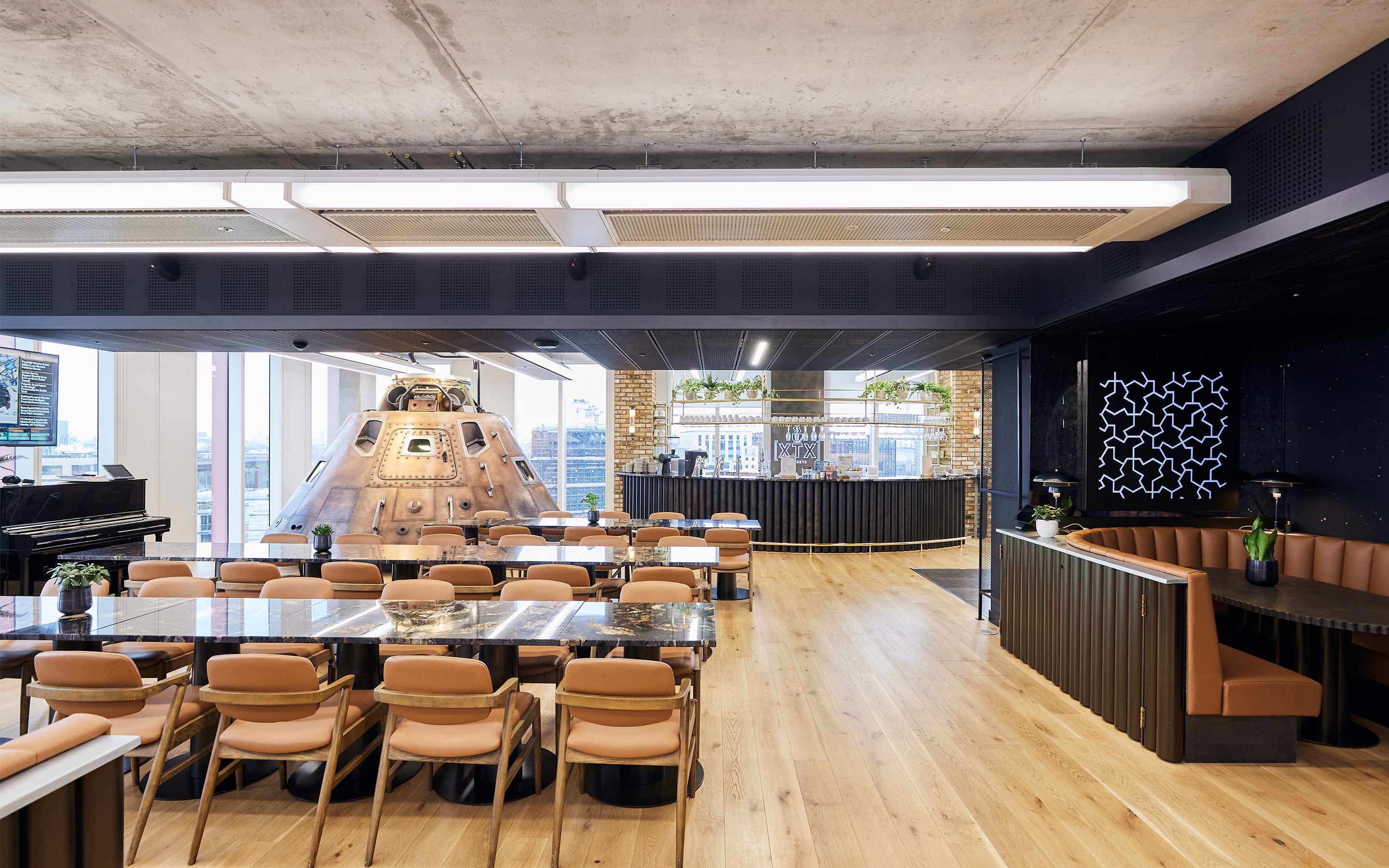 Office canteen with modern design, showcasing wooden floors, a barista bar, and leather chairs