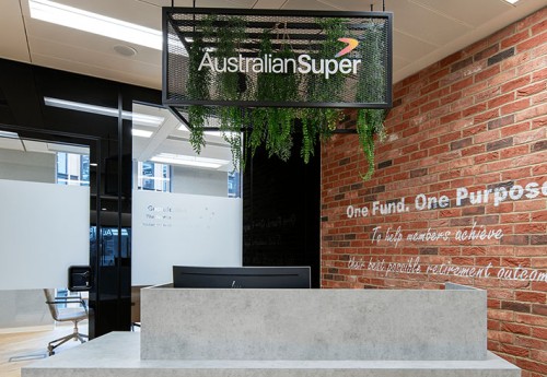 A blacked gated cube hung above a grey stone effect front desk with an exposed brick wall to the right and a glass walled office the back
