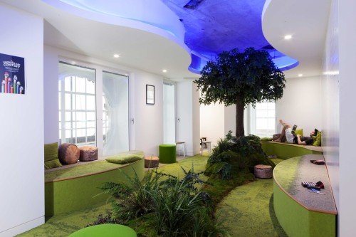 A white room with a green carpeted floor and biopillia going through the centre illuminated by a deep blue light carved out of the ceiling