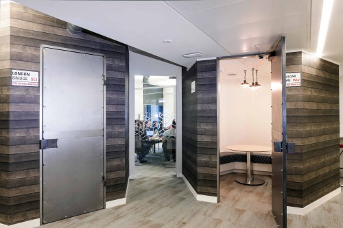 a hallway designed with dark wooden finished walls two steel metal doors on the left and right and a glass door in the centre that leads to a meeting room