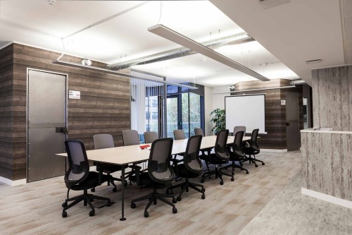 A light wooden finished boardroom table with black and grey chairs in the centre of dark wooden and grey wooden impression walls