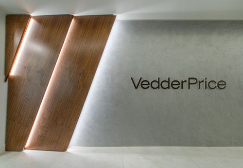 A grey wall with vedder prices' logo in black and 3 wooden slates with back lighting to the right